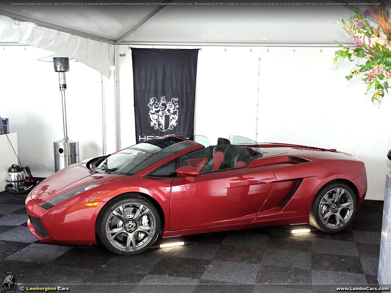 A striking red Lamborghini Gallardo Spyder displayed under a white event tent, highlighting its open-top design and aggressive stance.