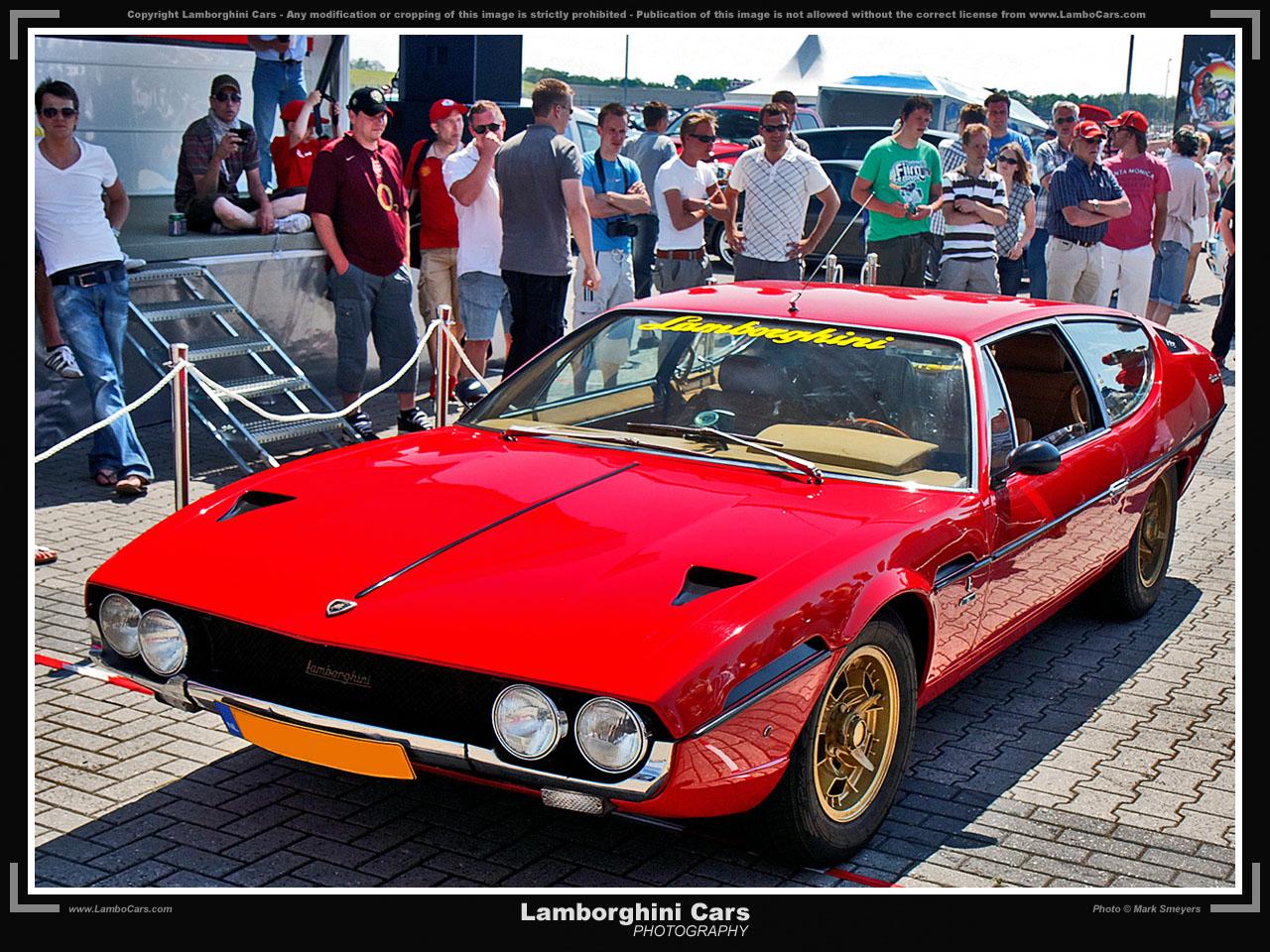 A striking red Lamborghini Espada, a classic 2+2 grand tourer, displayed at an outdoor car event with a crowd of spectators.