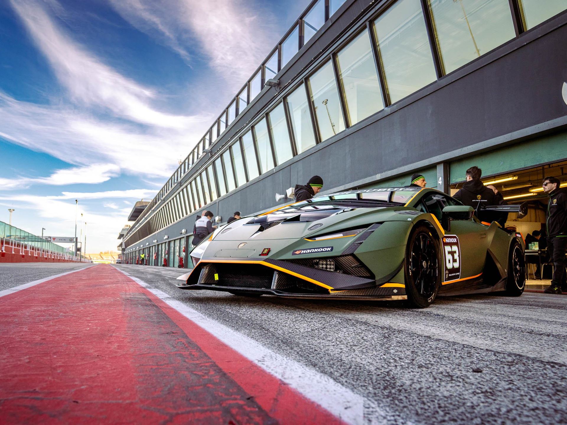 Lamborghini'S Talent Pipeline Delivers: Paul And Michelotto Earn Factory Seats, Cook And Queen Named Junior Winners 7 Green lamborghini race car number 63 with orange accents parked in the pit lane surrounded by team members under dramatic sky