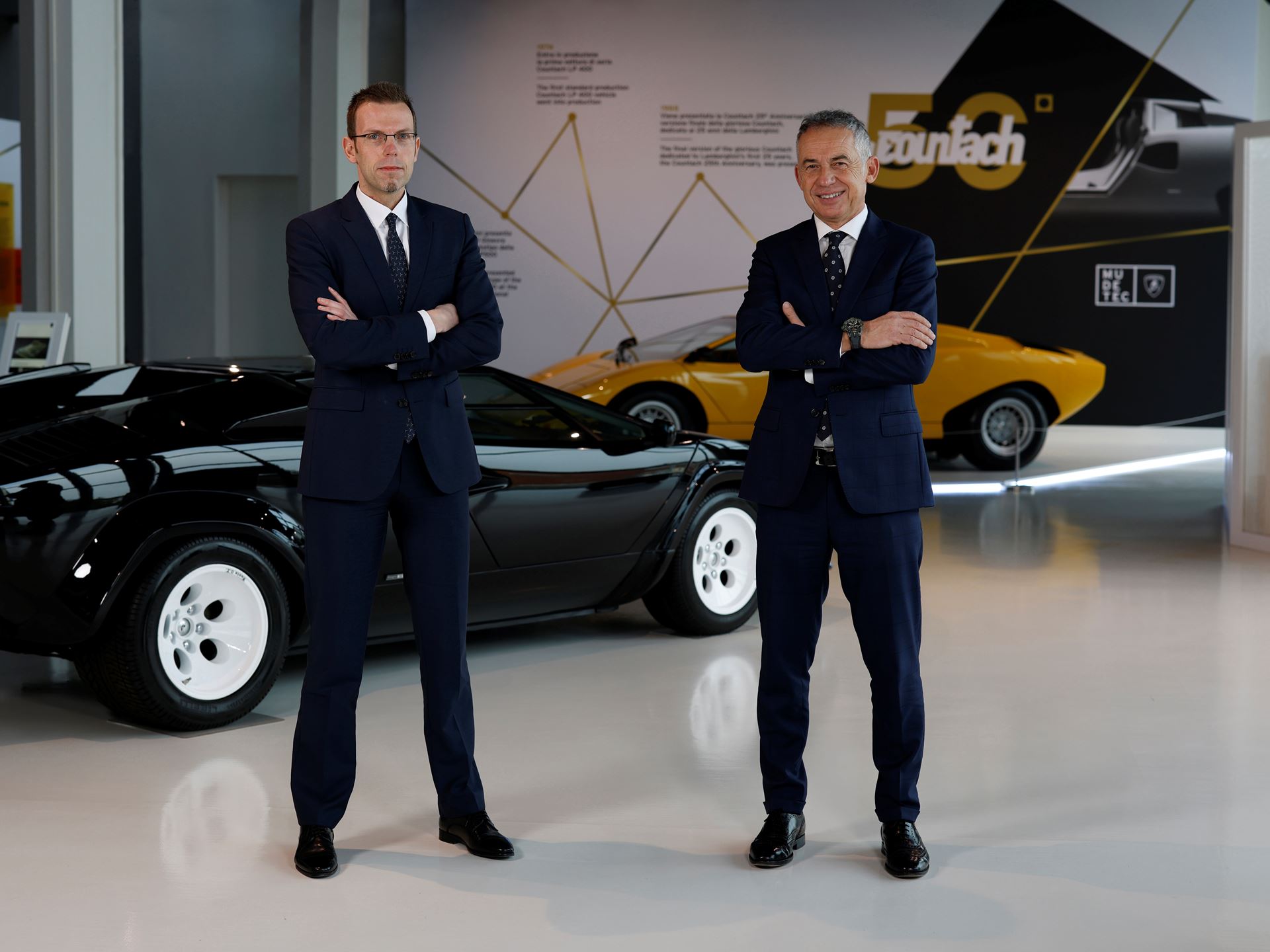 Lamborghini'S New Racing Boss Comes Straight From Ferrari'S Playbook, And The Timing Is No Coincidence 17 Two men in suits stand in front of a black lamborghini countach, with a yellow vintage countach and a modern countach lpi 800-4 visible in the background. The setting appears to be a showroom or museu