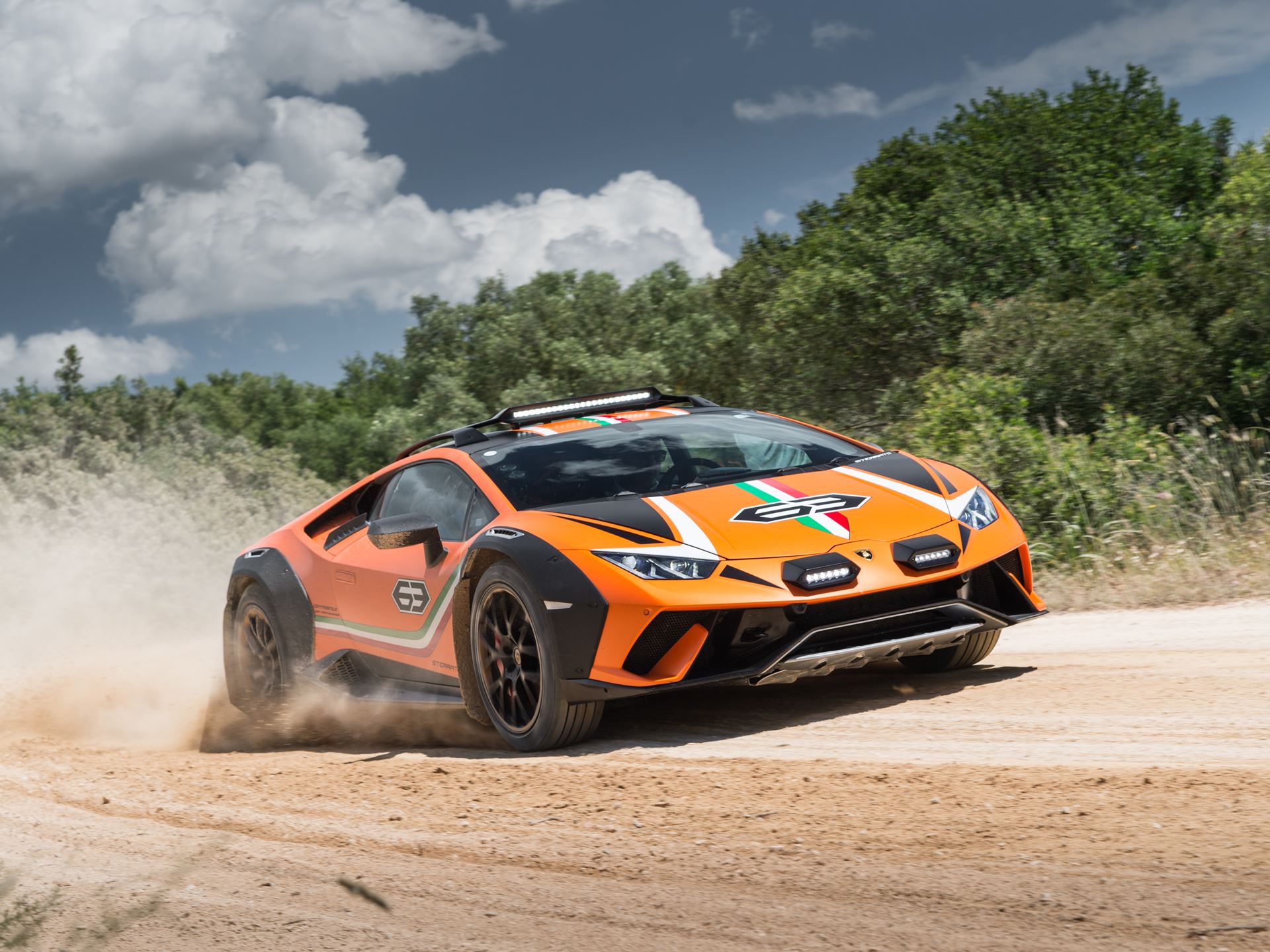 Lamborghini'S New Racing Boss Comes Straight From Ferrari'S Playbook, And The Timing Is No Coincidence 15 An orange lamborghini huracan sterrato kicks up dust as it drives on a dirt road, showcasing its off-road capabilities. The car features rally-style lights, roof rails, and black fender flares, set ag