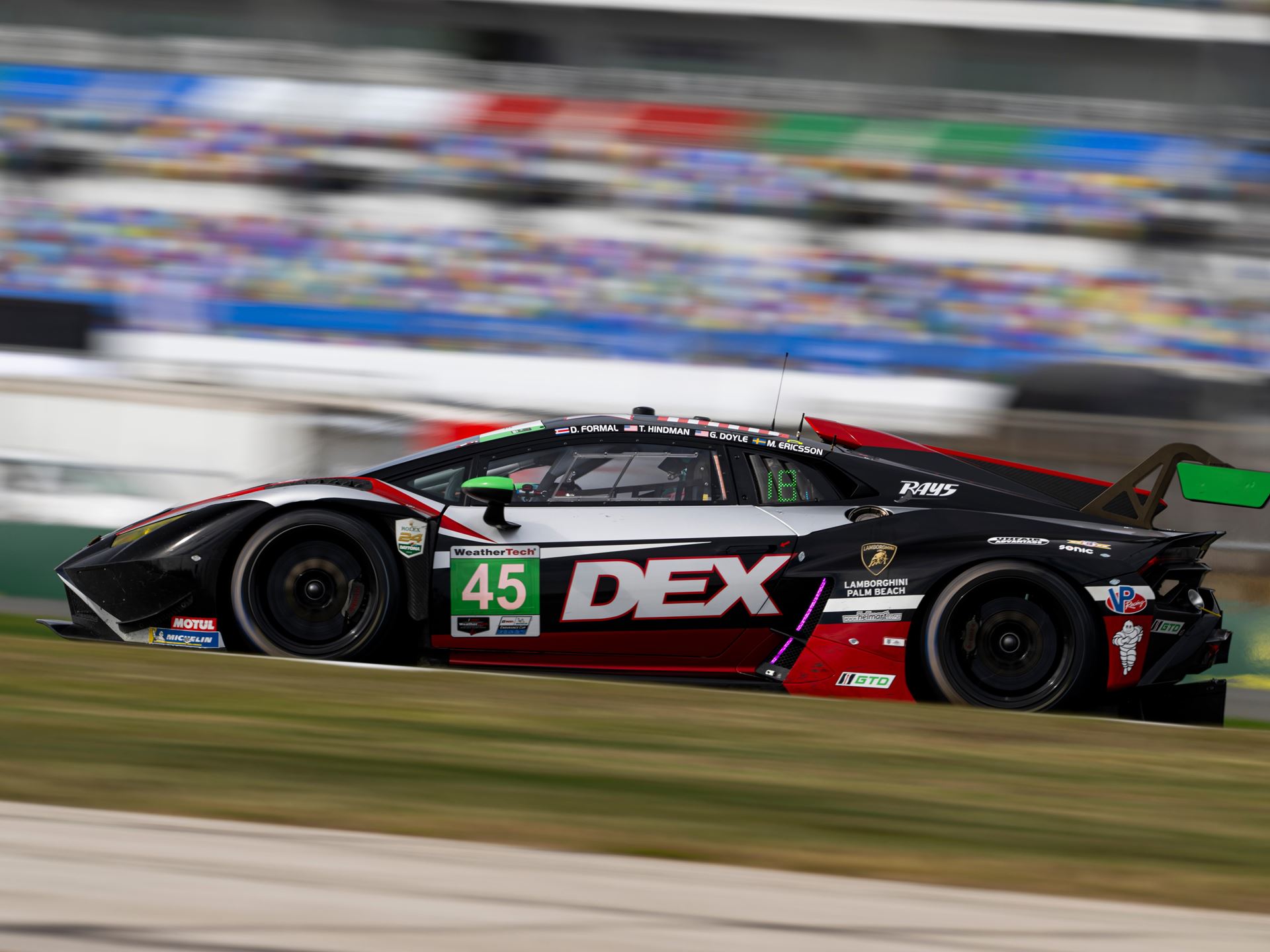 Lamborghini'S First In-House Gt3 Car Faces Brutal Sebring Debut 15 A lamborghini huracan gt3 evo race car, number 45, is in motion on a race track during daylight, with motion blur conveying speed. The car features a black, white, and red livery with green accents on