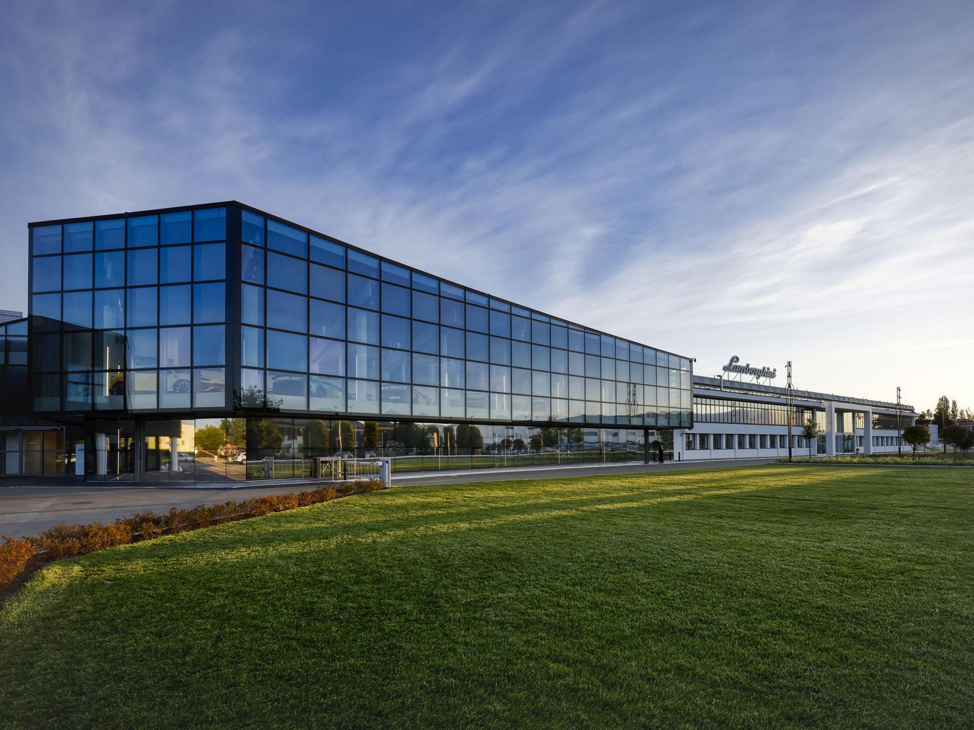 Exterior view of the modern, glass-fronted lamborghini headquarters building against a blue sky.