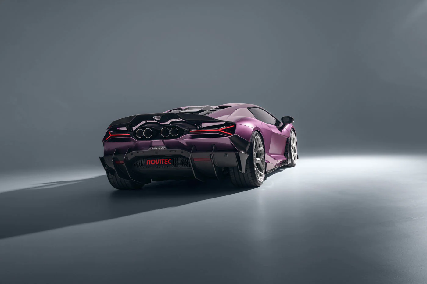 Novitec'S 1,048 Hp Revuelto Program: What It Offers That Lamborghini'S Own Ad Personam Cannot 37 A purple novitec lamborghini revuelto is shown from a 3/4 rear angle in a minimalist grey studio. The focus is on the car's intricate rear design, featuring its quad exhaust, aggressive diffuser, and