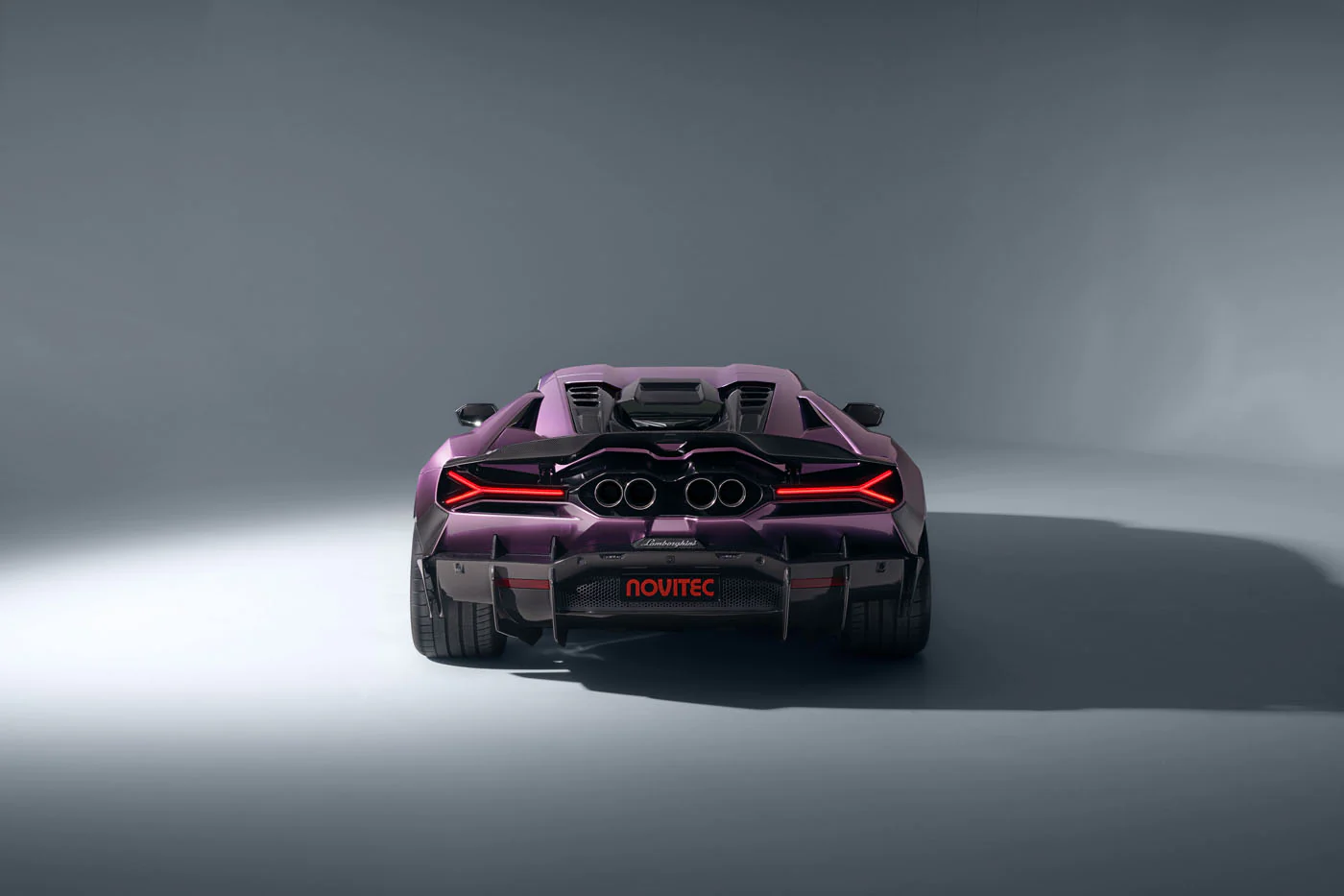 Novitec'S 1,048 Hp Revuelto Program: What It Offers That Lamborghini'S Own Ad Personam Cannot 41 A direct rear view of a purple novitec lamborghini revuelto in a grey studio setting. The image emphasizes the car's symmetrical and aggressive rear fascia, featuring its prominent quad exhaust, y-sha