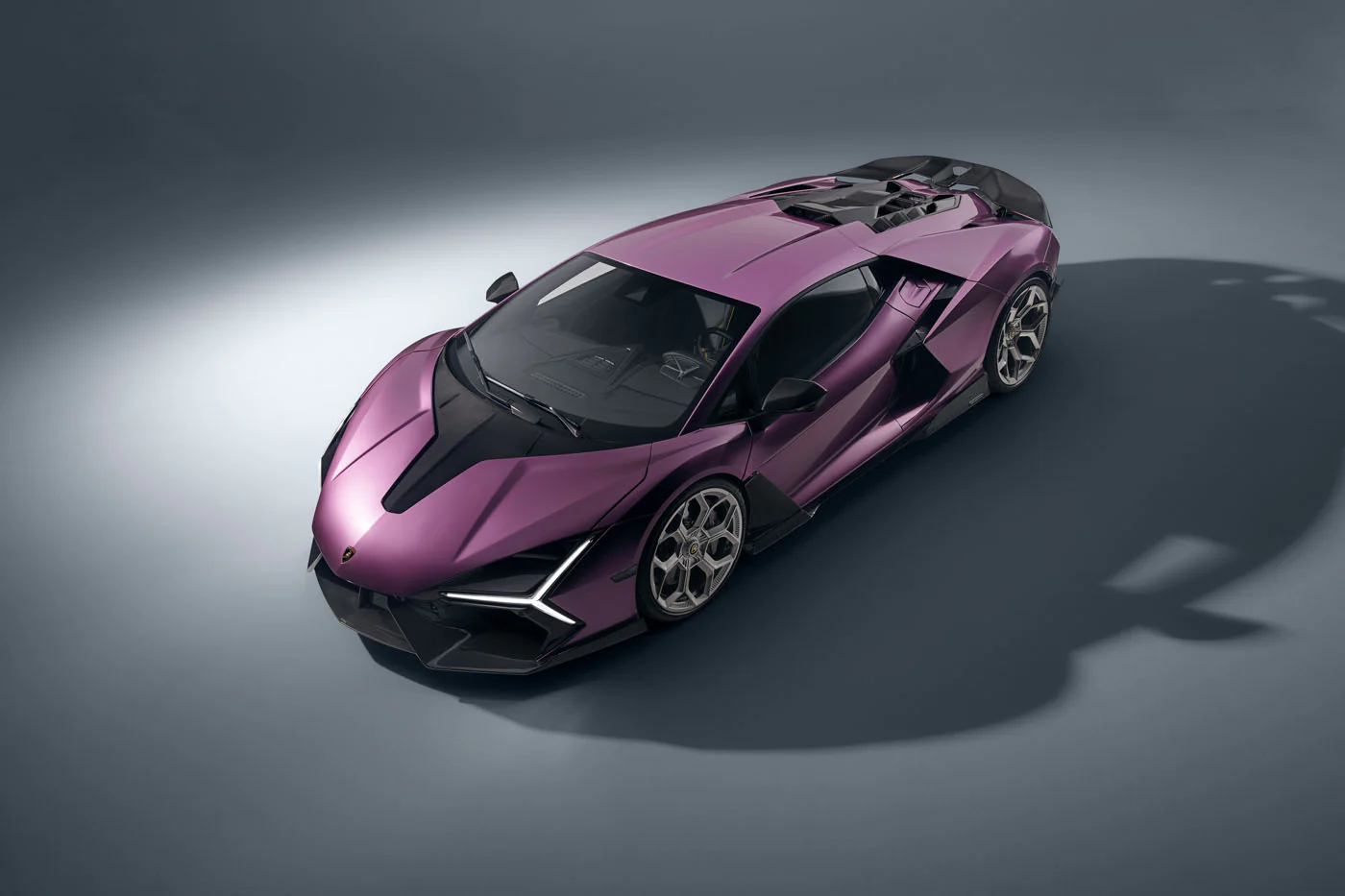 Novitec'S 1,048 Hp Revuelto Program: What It Offers That Lamborghini'S Own Ad Personam Cannot 27 An elevated top-down view of a purple lamborghini revuelto in a studio, showcasing its sleek roofline, engine cover, and the overall aerodynamic shape. The shadows cast by the car add depth to the com