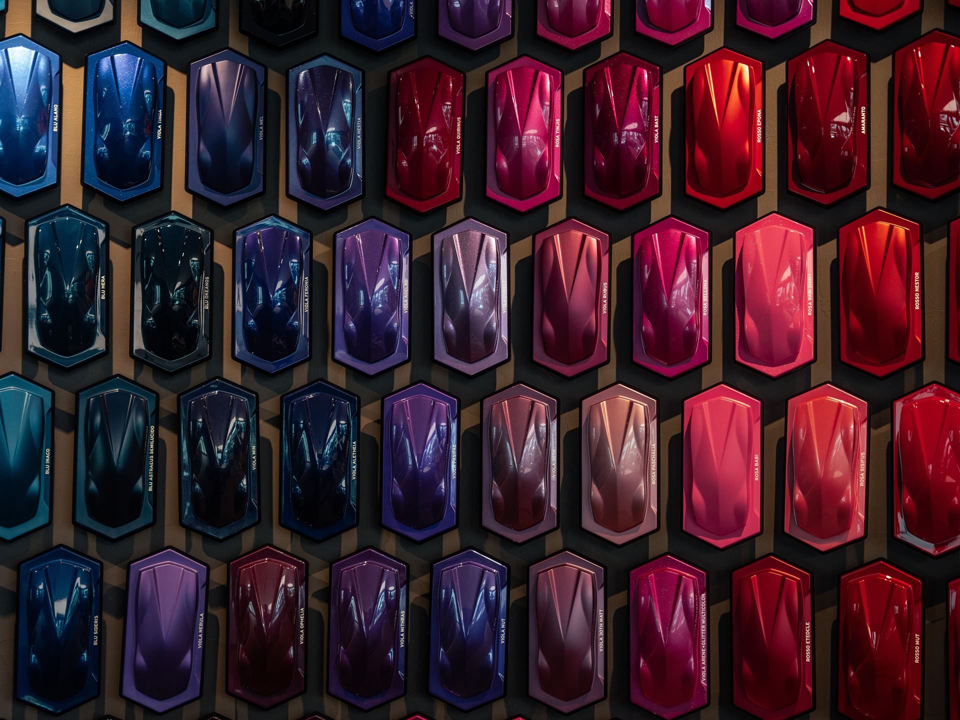 A wall display of hexagonal Lamborghini paint samples spanning a wide color spectrum from deep blues to vibrant reds