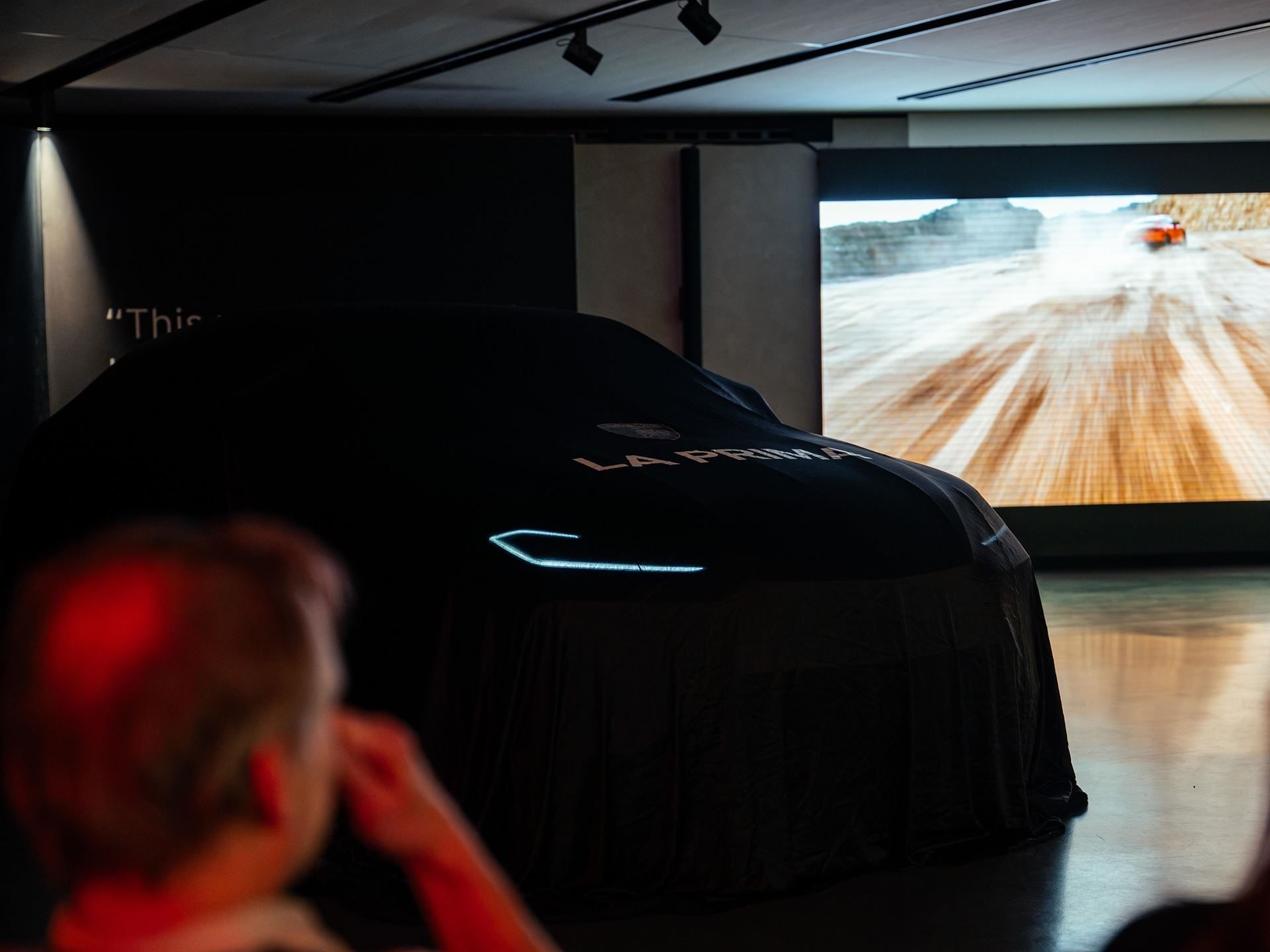 A Lamborghini covered by a black sheet with glowing LED daytime running lights during a La Prima unveiling event