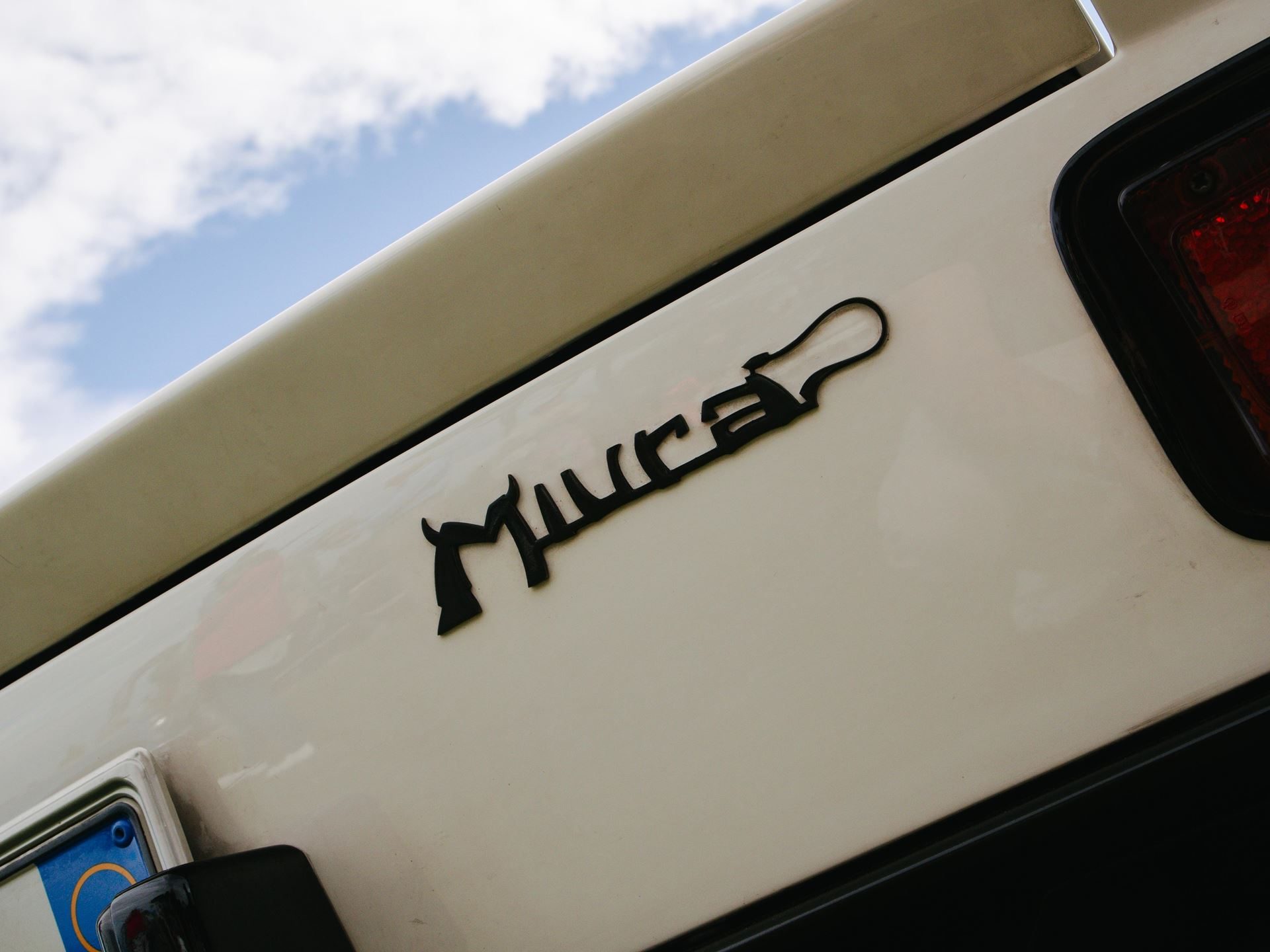 The Counterclockwise Crankshaft And Shared Sump That Invented The Supercar: 60 Years Of Lamborghini Miura 11 Close-up of the stylized miura script badge on the rear of a white lamborghini with reflections of blue sky