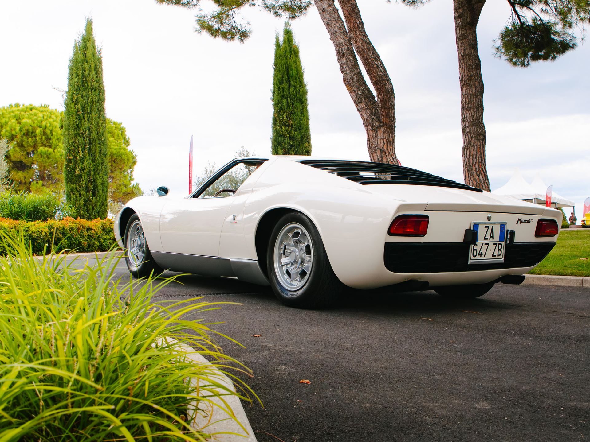 The Counterclockwise Crankshaft And Shared Sump That Invented The Supercar: 60 Years Of Lamborghini Miura 7 Pristine white lamborghini miura from a 3/4 rear angle showing distinctive rear louvers, wide stance, and classic five-hole wheels against lush greenery