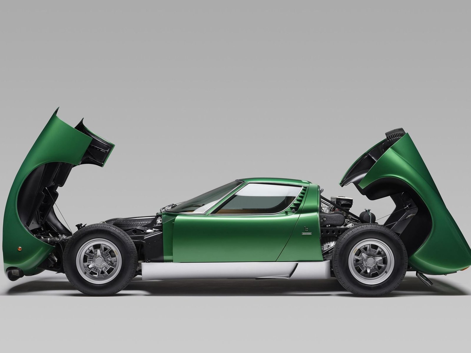 Green Lamborghini Miura with front and rear panels open revealing the transverse V12 engine, transaxle, and chassis structure