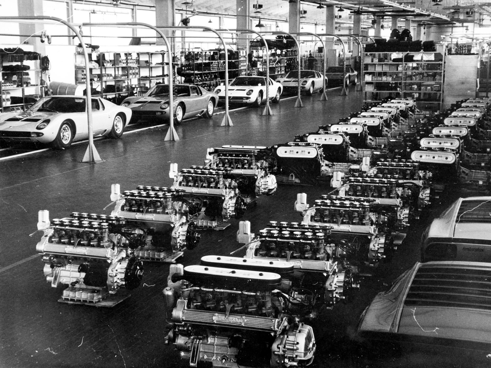 The Counterclockwise Crankshaft And Shared Sump That Invented The Supercar: 60 Years Of Lamborghini Miura 3 Black and white archival photo of the lamborghini factory floor showing rows of miura chassis, v12 engines in assembly, and completed body shells in the background
