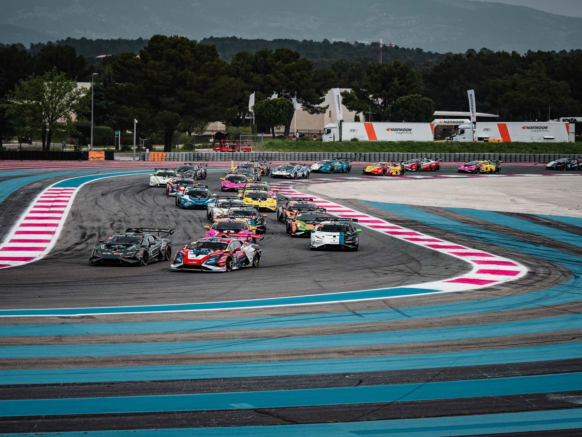 Numerous lamborghini huracán super trofeo evo2 race cars navigate a tight multi-apex corner at paul ricard, displaying a kaleidoscope of team liveries