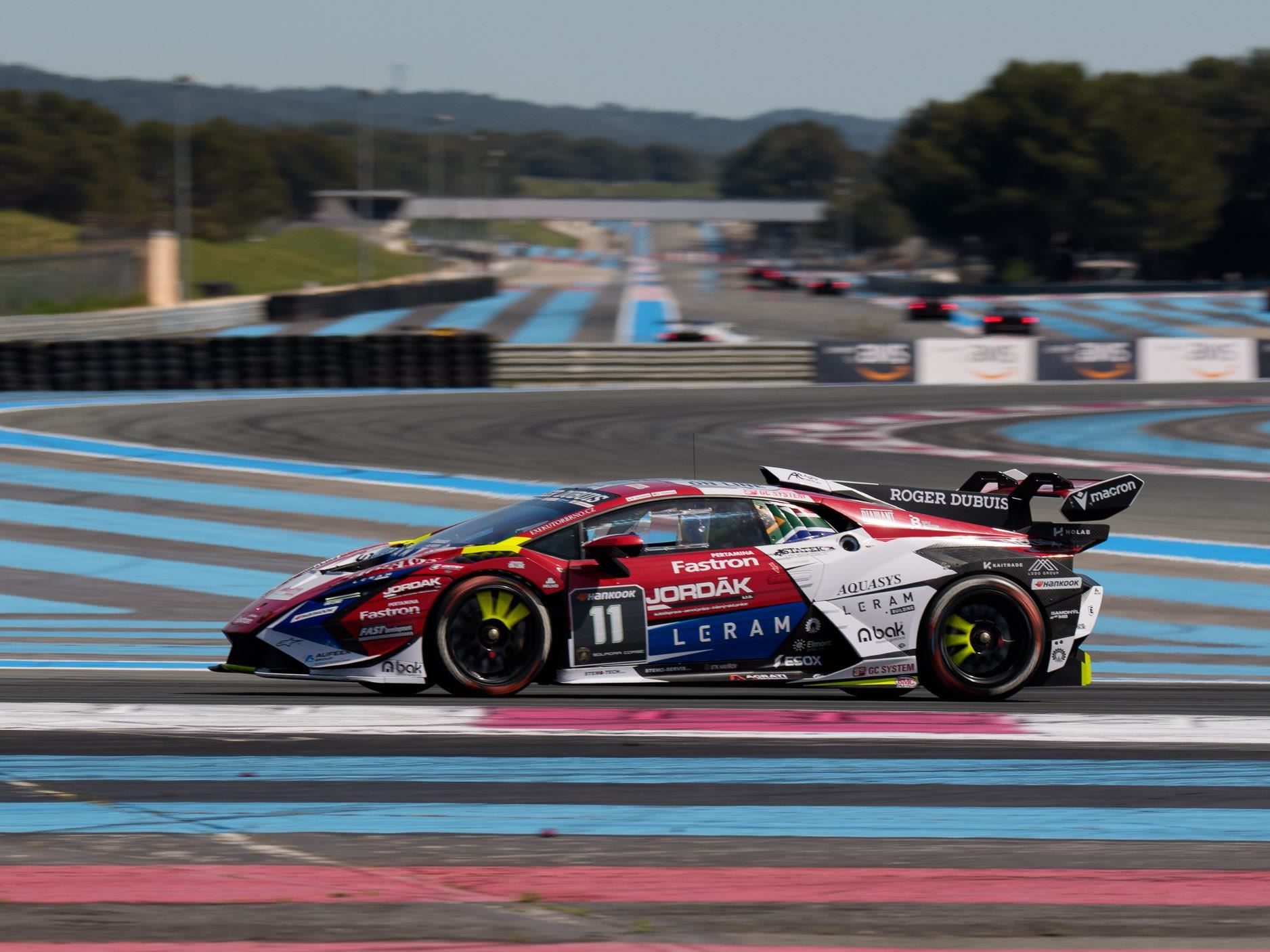 A red, white, and black lamborghini huracán super trofeo evo2 number 11 speeds through a paul ricard turn with its prominent rear wing and side vents highlighted against a clear blue sky