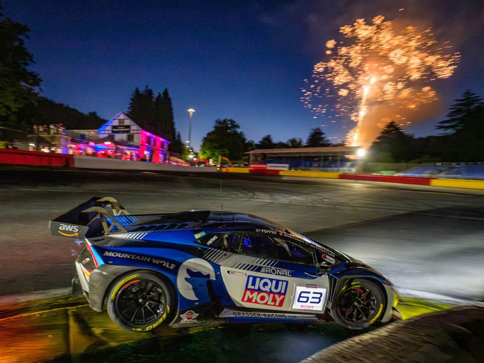 Lamborghini Huracán GT3 EVO race car number 63 racing at night with fireworks in the background