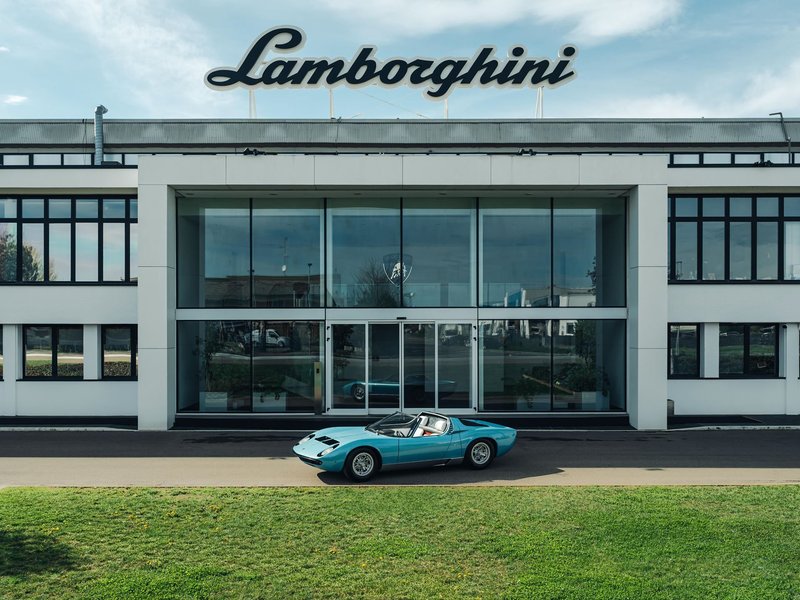 Classic light blue Lamborghini Miura parked in front of the modern Lamborghini factory in Sant'Agata Bolognese