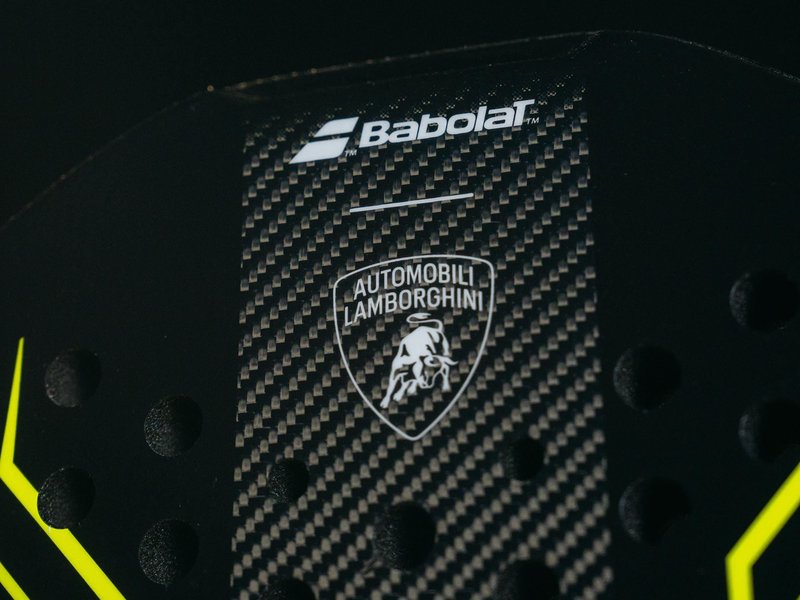 Close-up of the Babolat x Lamborghini BL002 padel racquet head showing the Automobili Lamborghini logo on a carbon fiber surface with yellow accents
