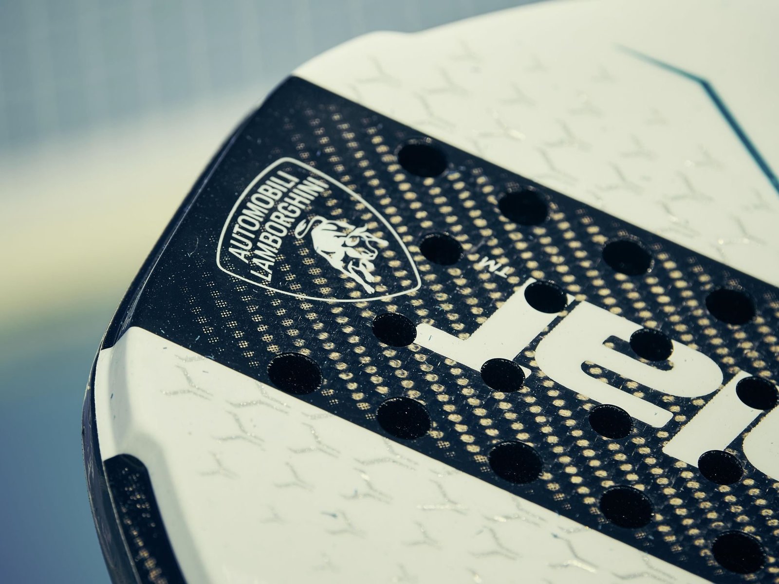 Extreme close-up of the Lamborghini shield logo on the white BL003 padel racquet showing visible carbon fiber texture