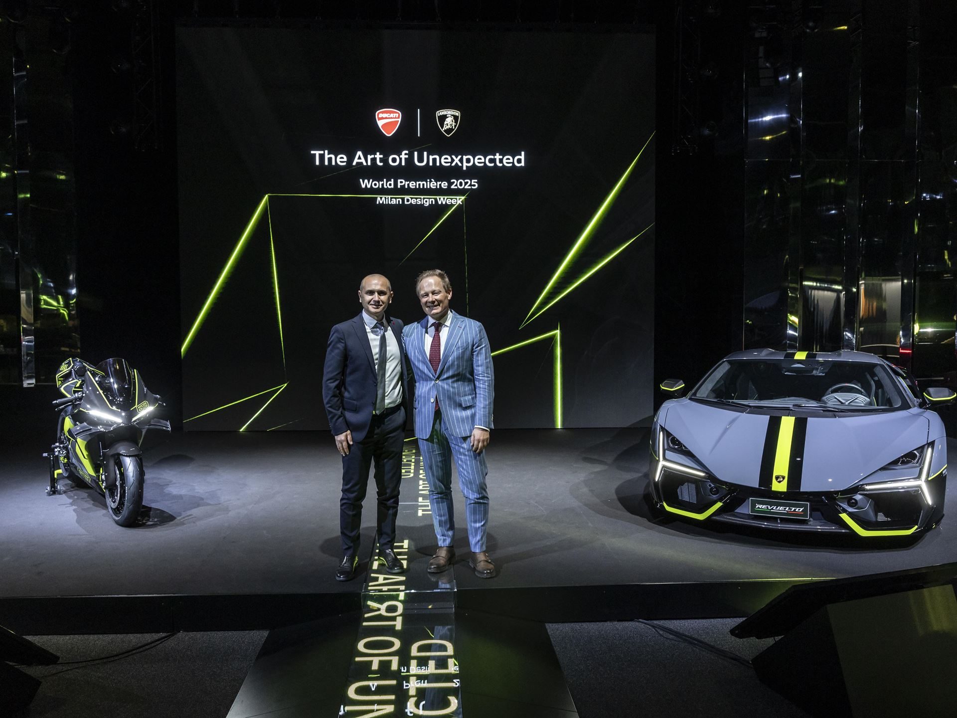 Ducati'S Panigale V4 Lamborghini Lets 63 Revuelto Owners Build A Matching Two-Wheel Garage 3 Two executives standing between the lamborghini revuelto and ducati panigale v4 lamborghini in matching grey and verde scandal livery at the milan design week reveal