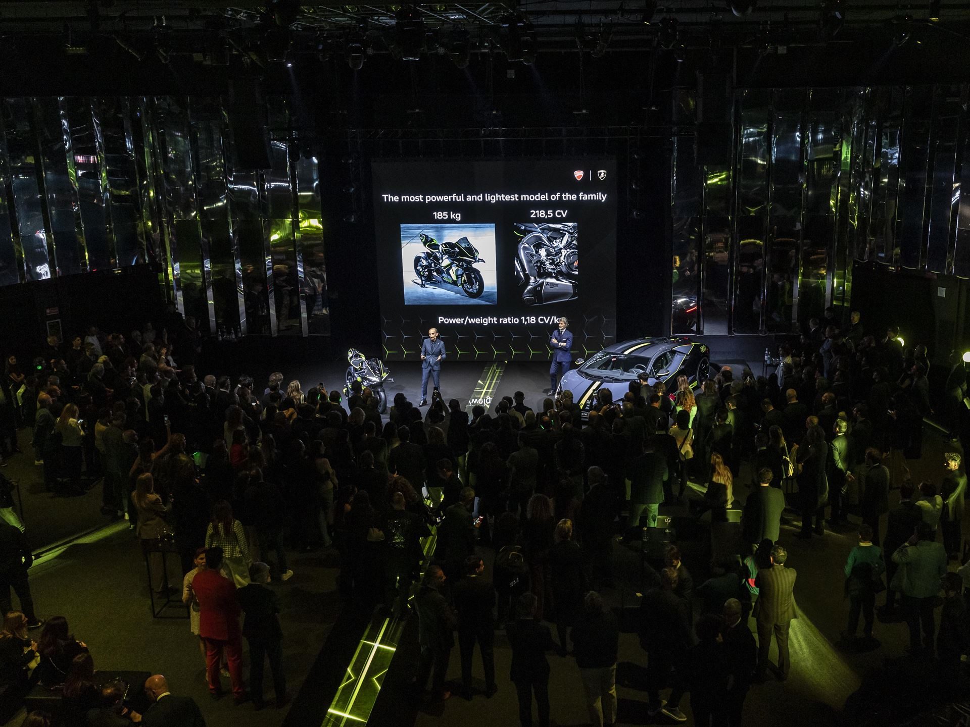 Ducati'S Panigale V4 Lamborghini Lets 63 Revuelto Owners Build A Matching Two-Wheel Garage 11 High-angle view of the milan design week reveal event showing the revuelto and panigale v4 lamborghini on stage with a large audience and screen displaying performance specifications