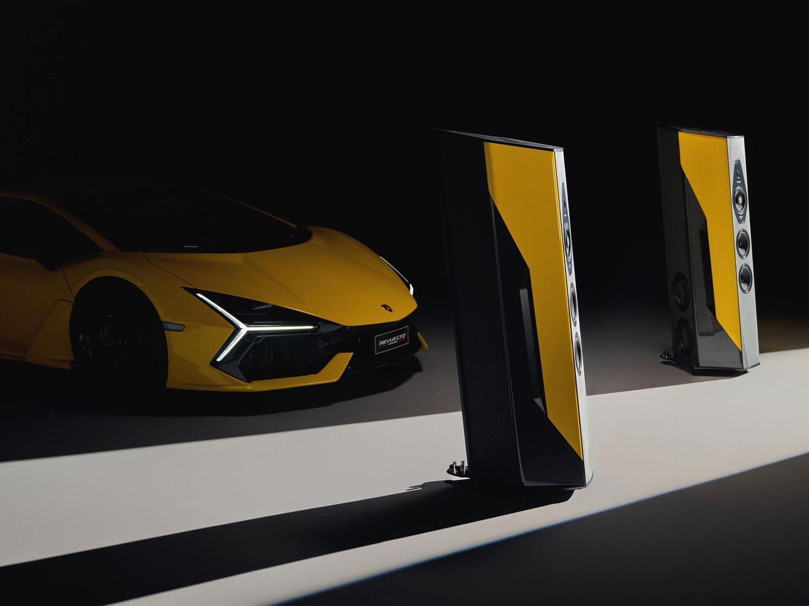 Sonus faber Il Cremonese Ex3me Automobili Lamborghini Edition speakers in Giallo Countach flanking a yellow Lamborghini Revuelto in a dark studio