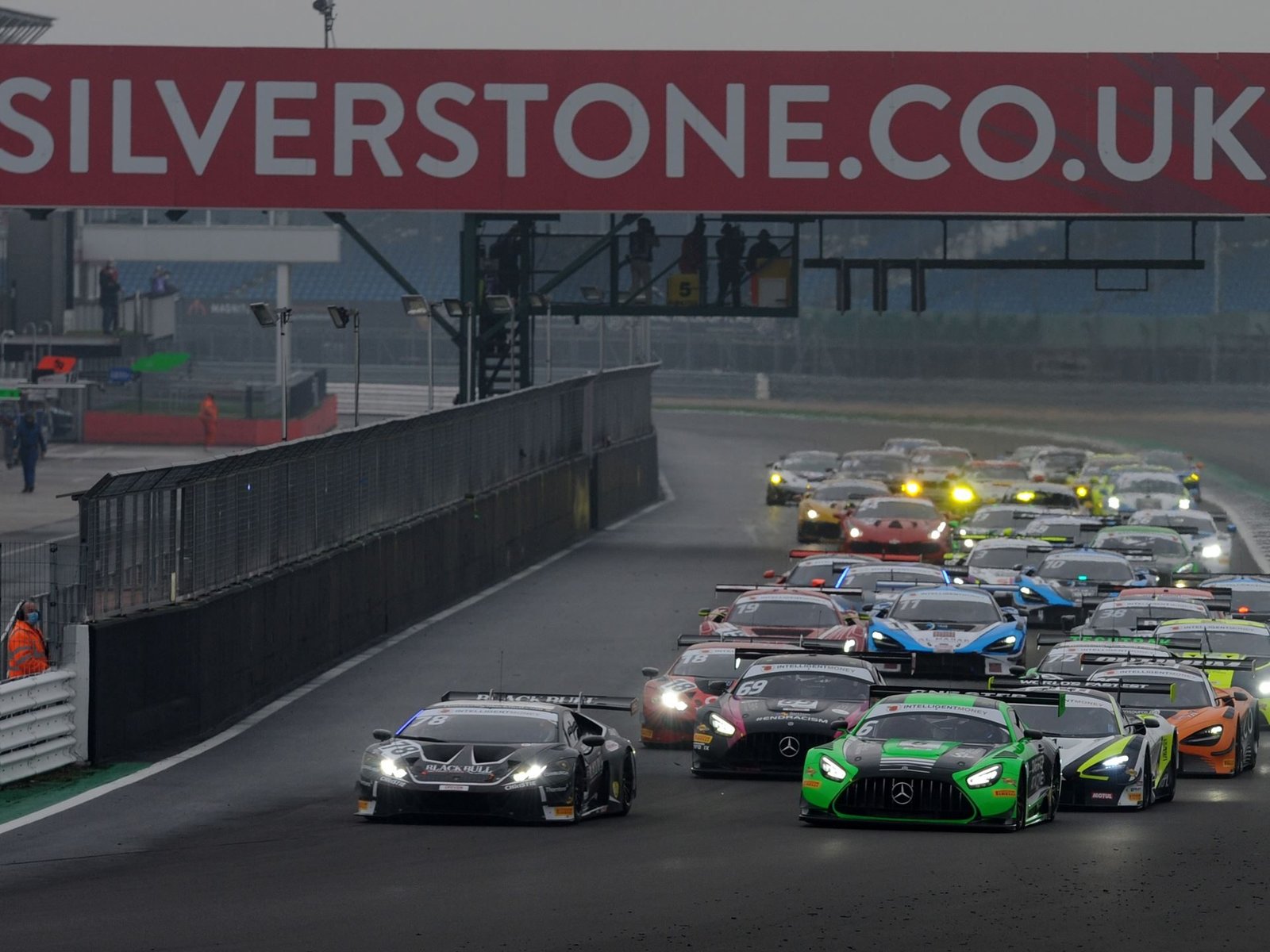 Black Lamborghini Huracán GT3 Evo leading a pack of GT cars on a wet Silverstone circuit under the Silverstone.co.uk banner