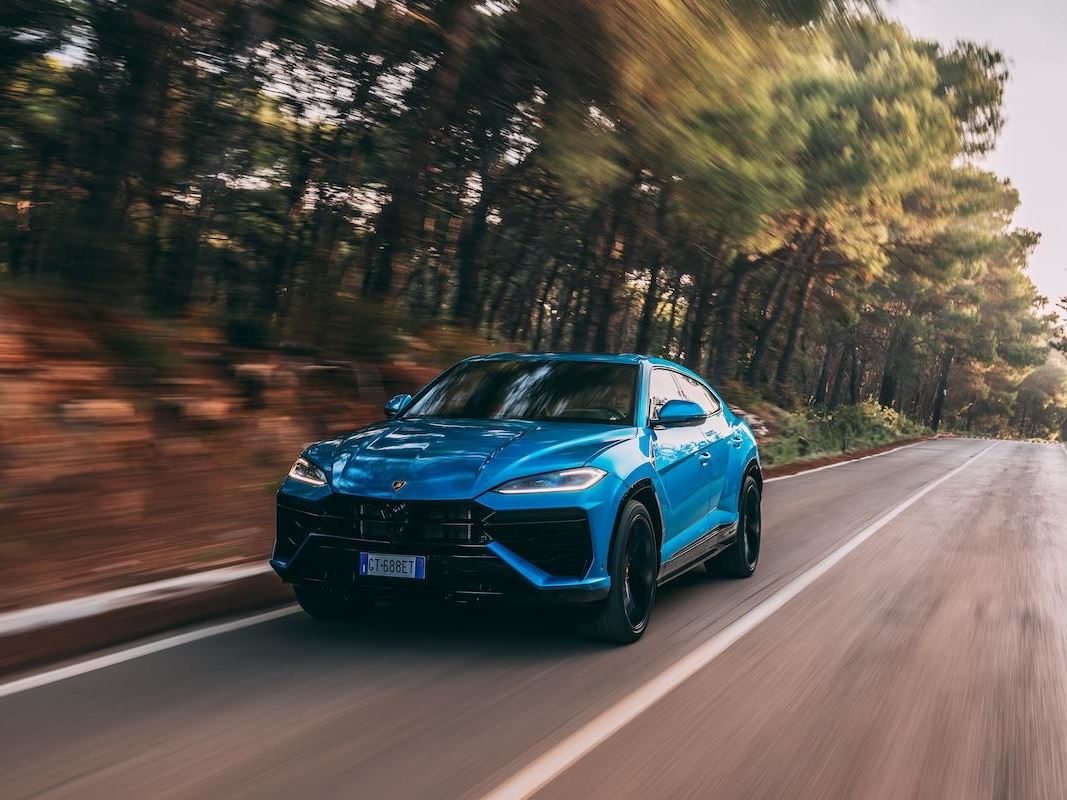 Blue Lamborghini Urus driving dynamically on a winding forest road with motion blur