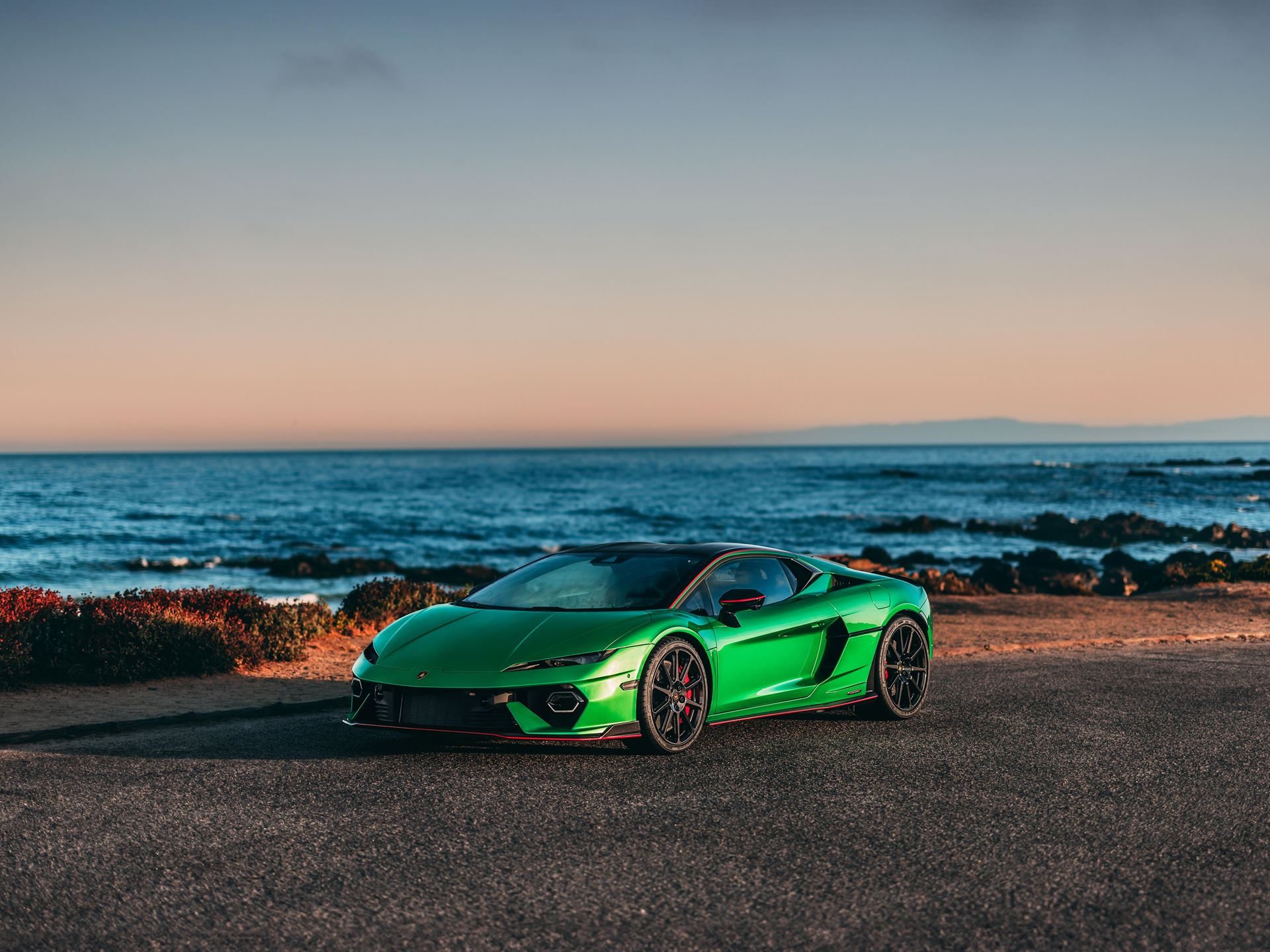 Green Lamborghini Revuelto parked on a coastal road with ocean and sunset in the background
