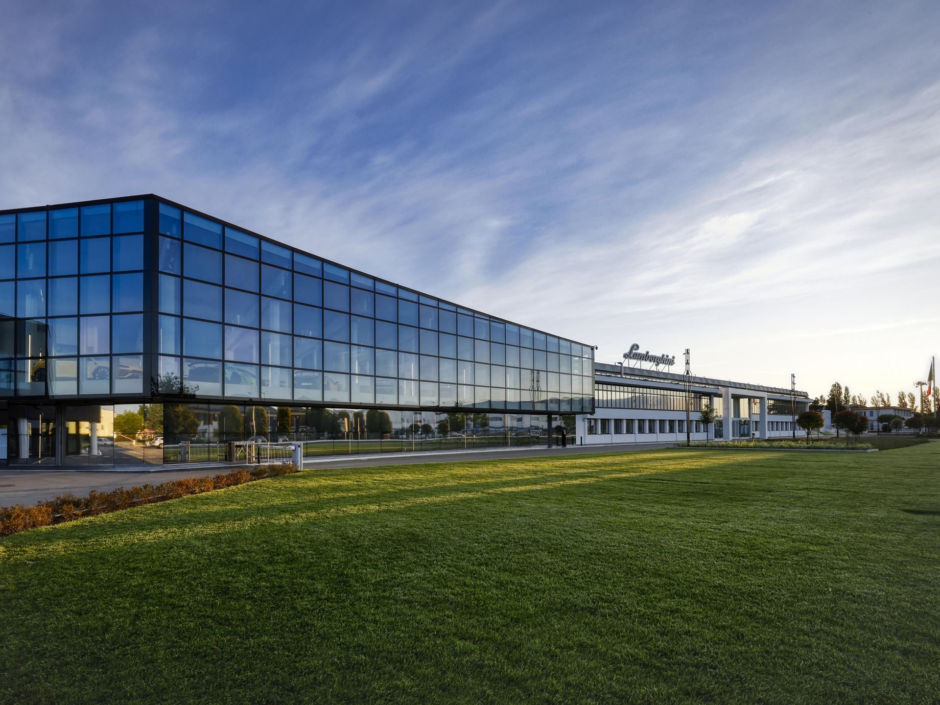 Exterior view of the modern Lamborghini factory in Sant'Agata Bolognese with large glass windows and the Lamborghini logo on the roof