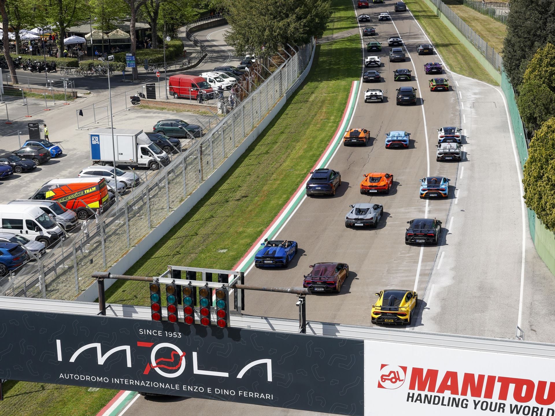 Elevated view of a line of diverse lamborghini models driving on the imola race track past the start/finish gantry