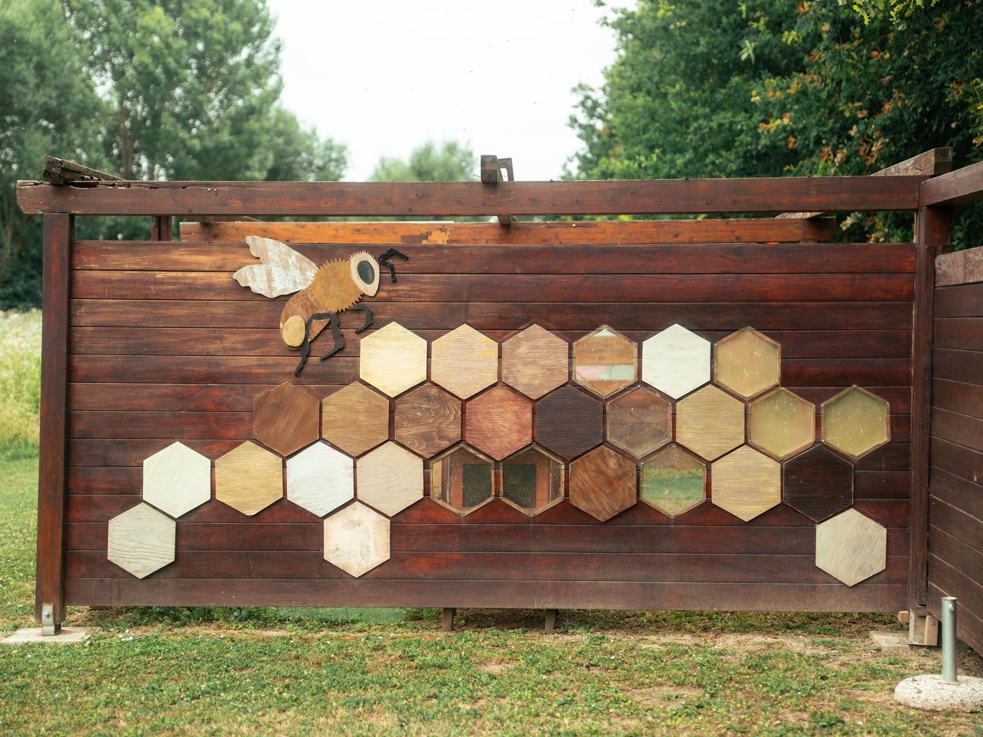 800,000 Bees And A Jar Of Honey: Inside Lamborghini'S Decade-Long Environmental Experiment 11 A decorative wooden fence with a large bee cutout and hexagonal honeycomb-patterned panels in various wood tones