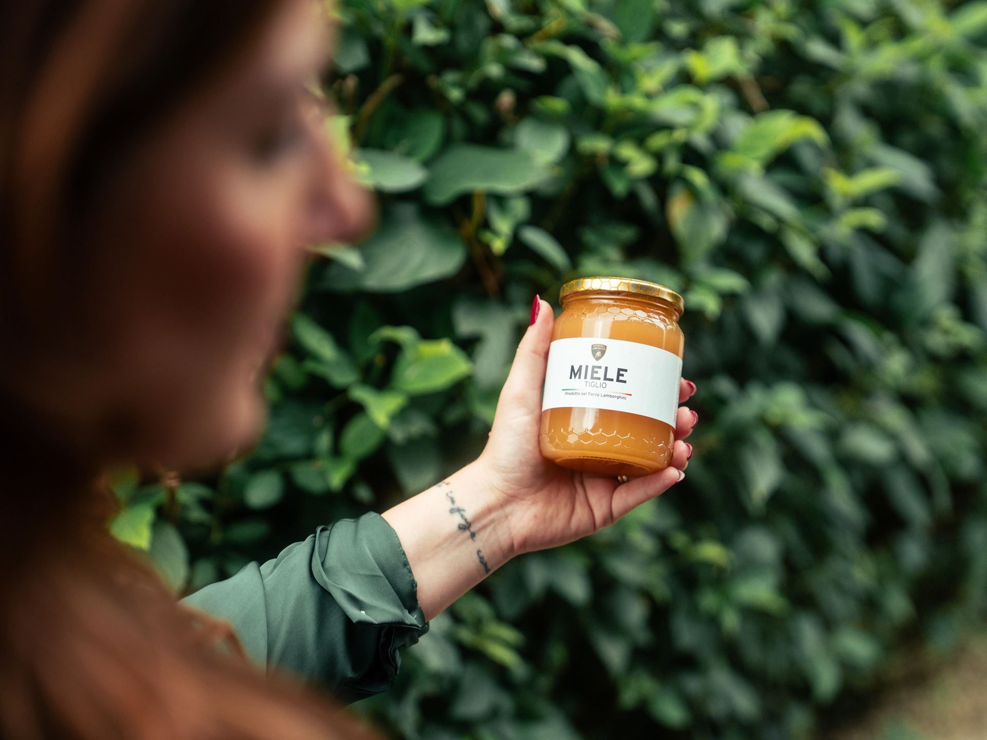 800,000 Bees And A Jar Of Honey: Inside Lamborghini'S Decade-Long Environmental Experiment 7 A hand holding a jar of lamborghini-branded miele honey with the lamborghini crest on the label against a green background