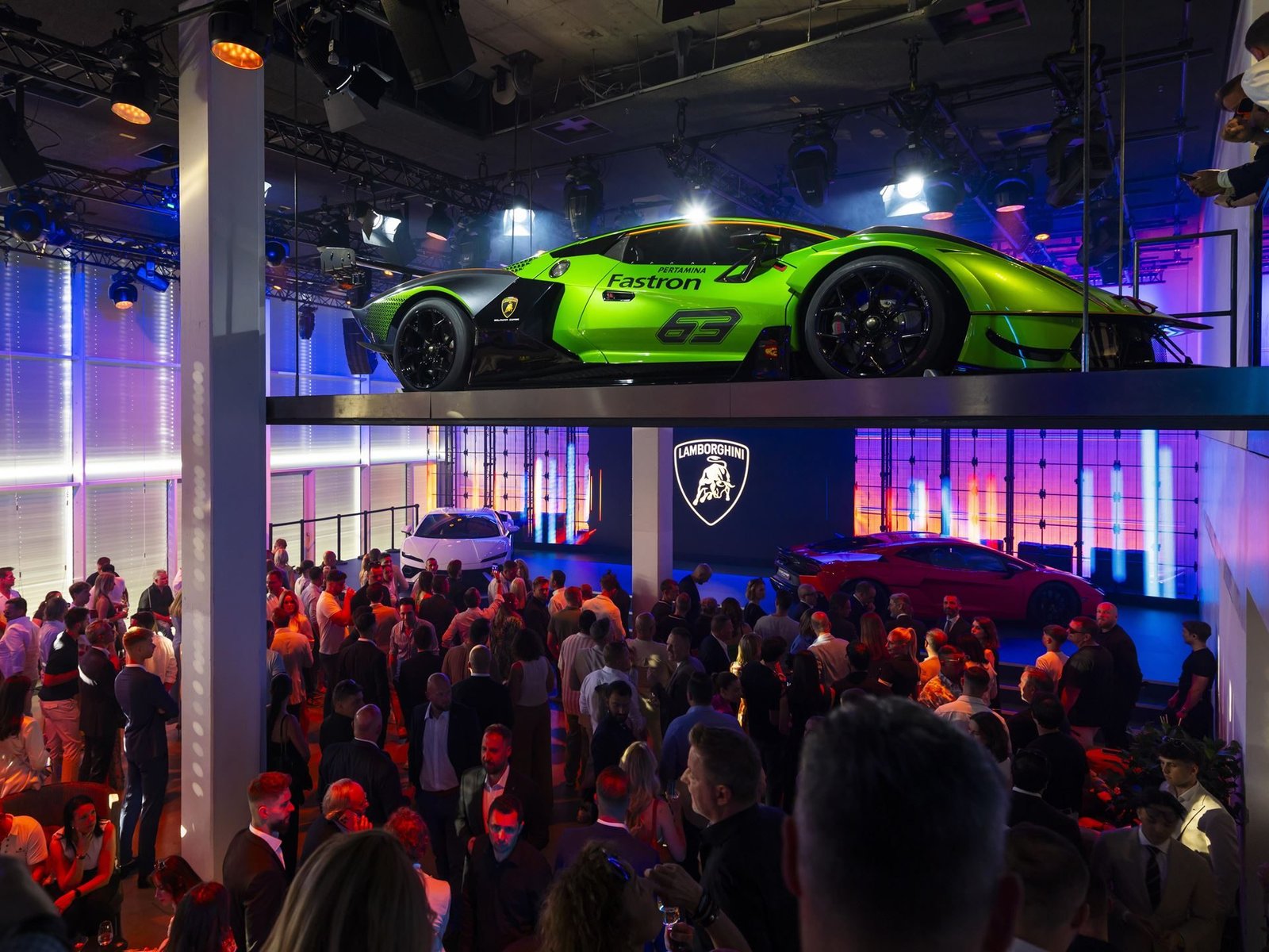 Indoor display at Lamborghini Day Germany 2025 showing a green Essenza SCV12 on an elevated platform alongside a white Revuelto and a crowd of guests
