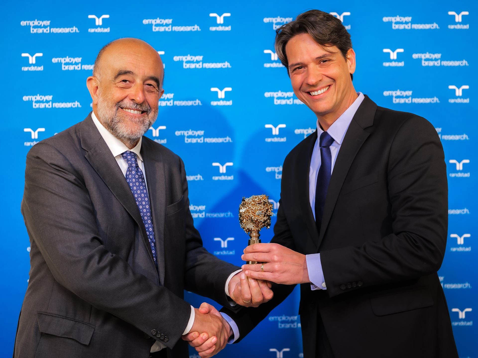 Italy'S Most Desired Employer Builds Supercars: What Lamborghini'S 79.8% Approval Rating Really Means 3 Two men shaking hands and holding the golden randstad employer brand award against blue randstad branding