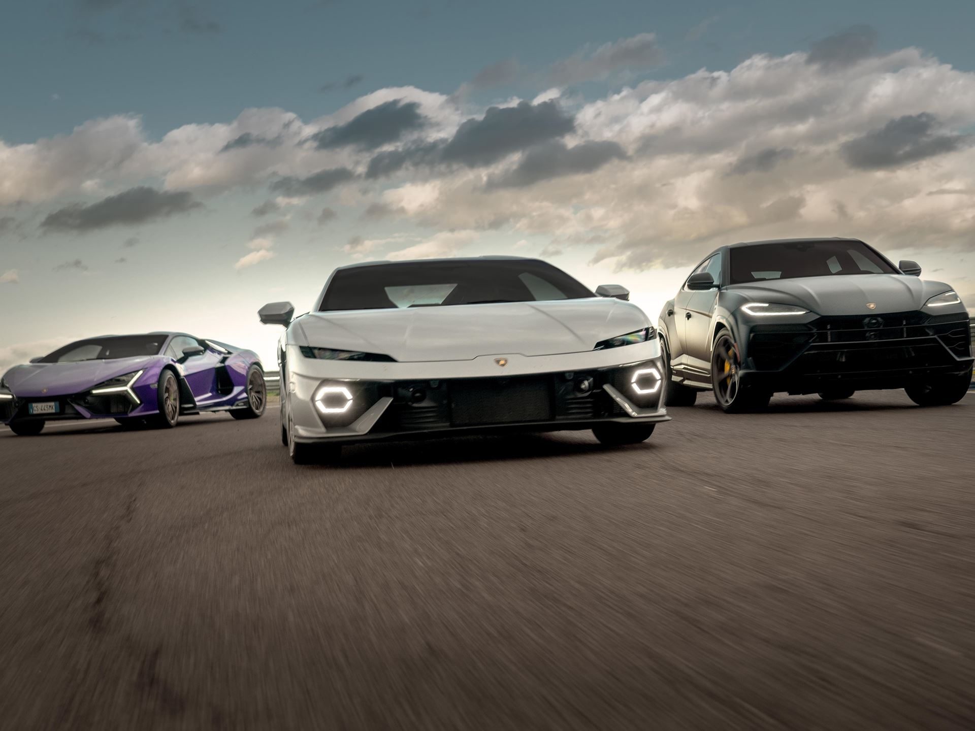 Lamborghini'S First Sustainability Report Reveals A Paradox: Emissions Rose While Every Car Went Hybrid 3 White lamborghini revuelto, purple huracán, and black urus driving in formation on a road under cloudy skies