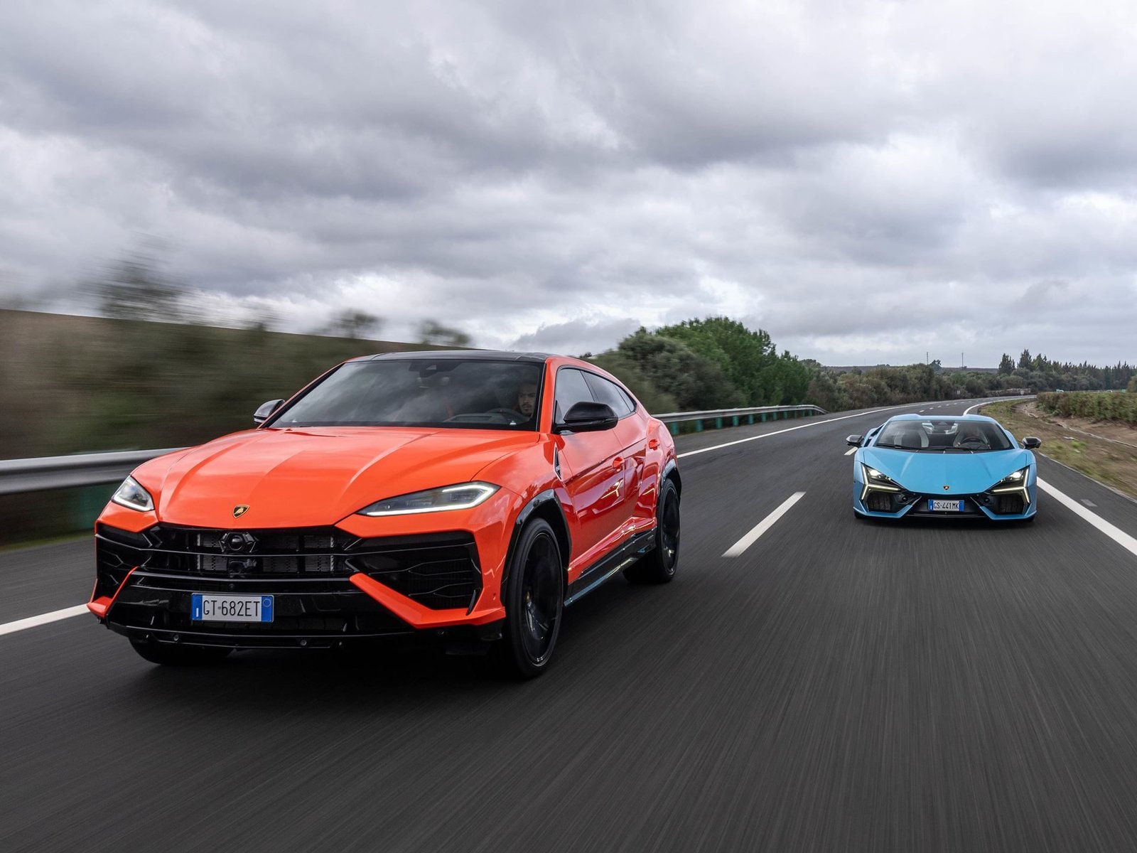 Orange Lamborghini Urus SE and blue Lamborghini Revuelto driving side by side on a highway
