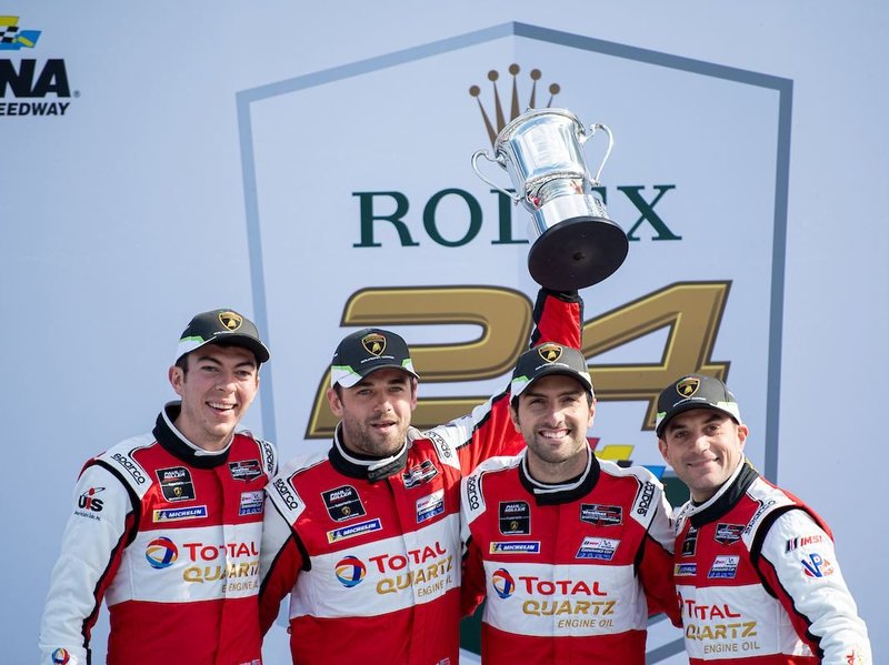 Paul Miller Racing drivers celebrate on the podium in Lamborghini racing suits with a trophy at the Rolex 24 at Daytona
