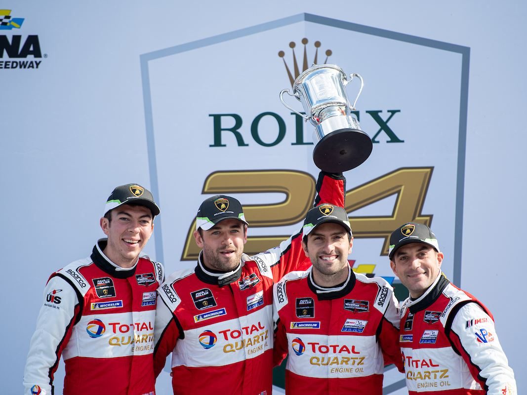 Paul miller racing drivers celebrate on the podium in lamborghini racing suits with a trophy at the rolex 24 at daytona