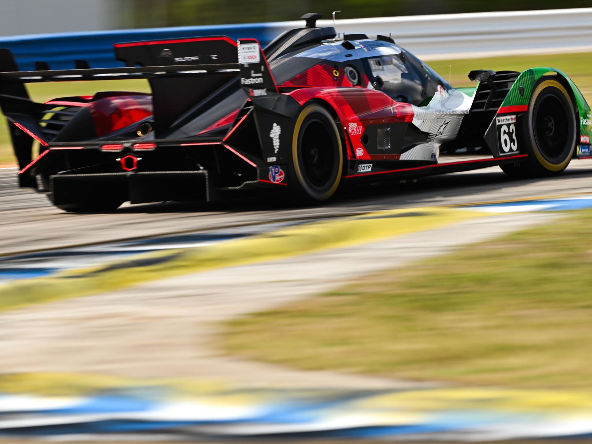 The #63 lamborghini sc63 lmdh prototype in red, black, and green livery cornering at sebring with complex rear aerodynamic elements visible