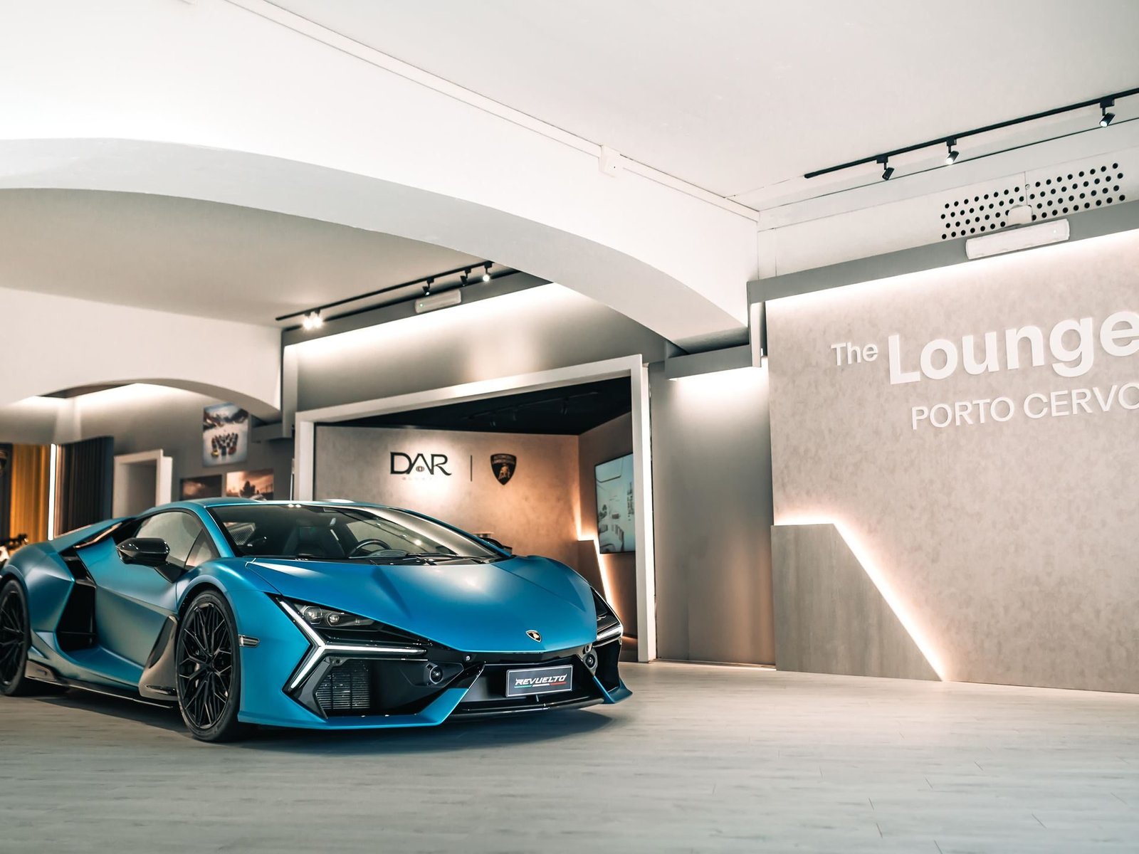 Matte blue Lamborghini Revuelto displayed inside the Porto Cervo Lounge with The Lounge Porto Cervo neon sign visible