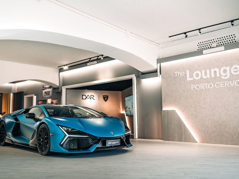 Matte blue Lamborghini Revuelto displayed inside the Porto Cervo Lounge with The Lounge Porto Cervo neon sign visible