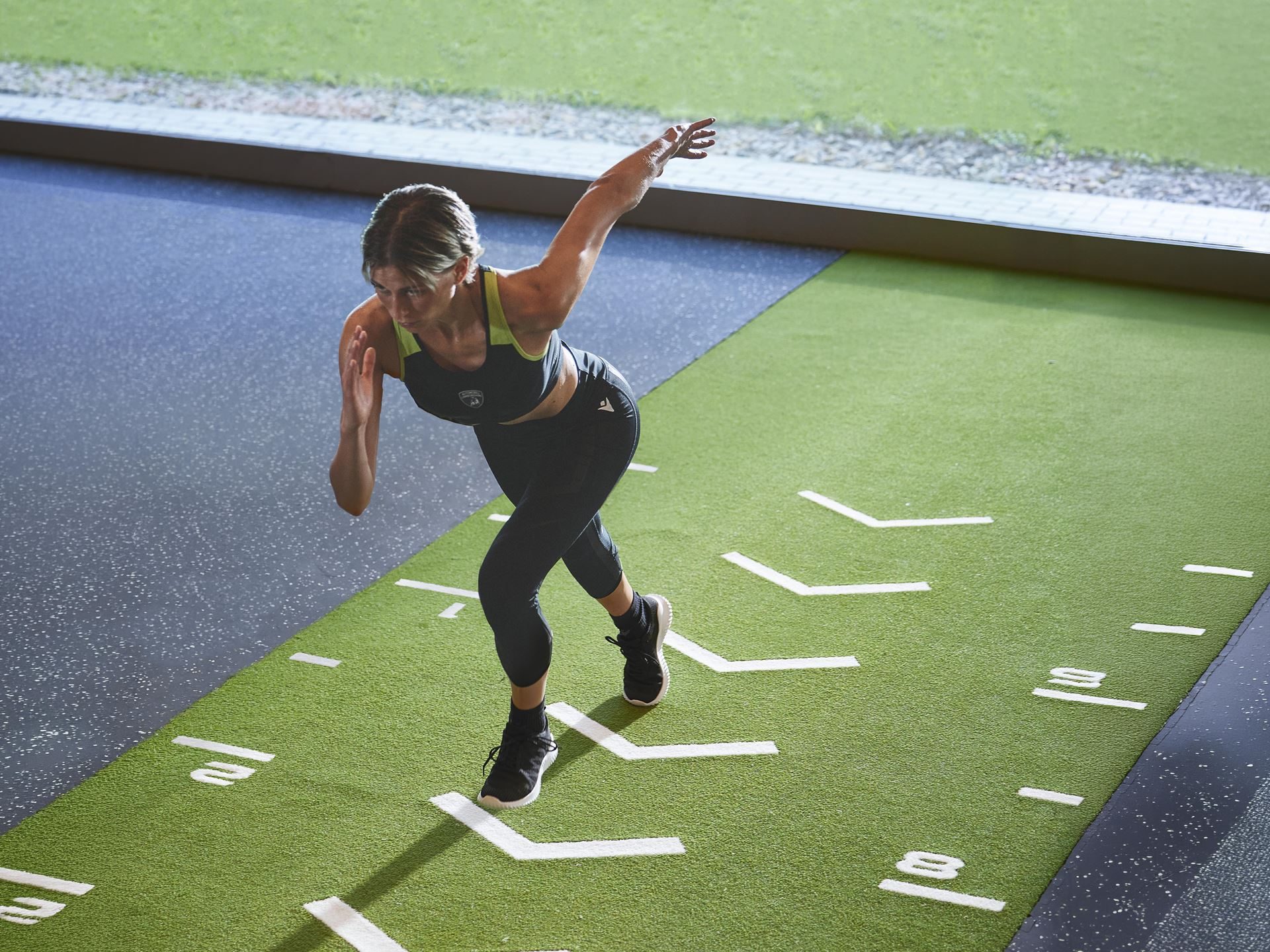 Lamborghini And Macron'S Second Activewear Drop Brings Sant'Agata'S Dna Into The Gym 11 Female model sprinting on indoor track wearing black lamborghini-branded macron activewear