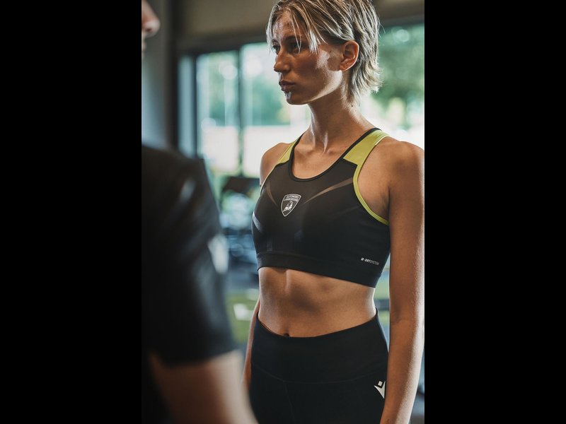 Close-up of female model wearing black Lamborghini-branded Macron sports bra with neon yellow accents and shield logo