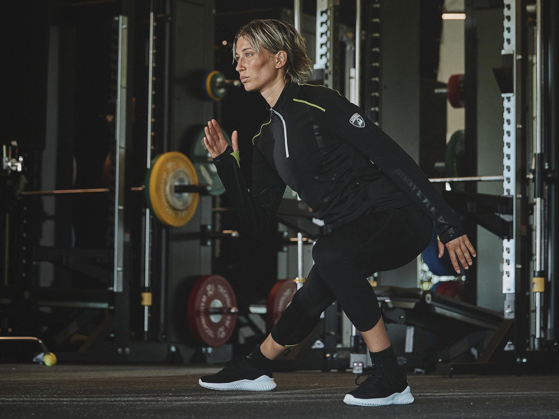 Lamborghini And Macron'S Second Activewear Drop Brings Sant'Agata'S Dna Into The Gym 7 Female model in dynamic pose wearing black long-sleeved half-zip lamborghini macron activewear top and leggings with neon yellow accents