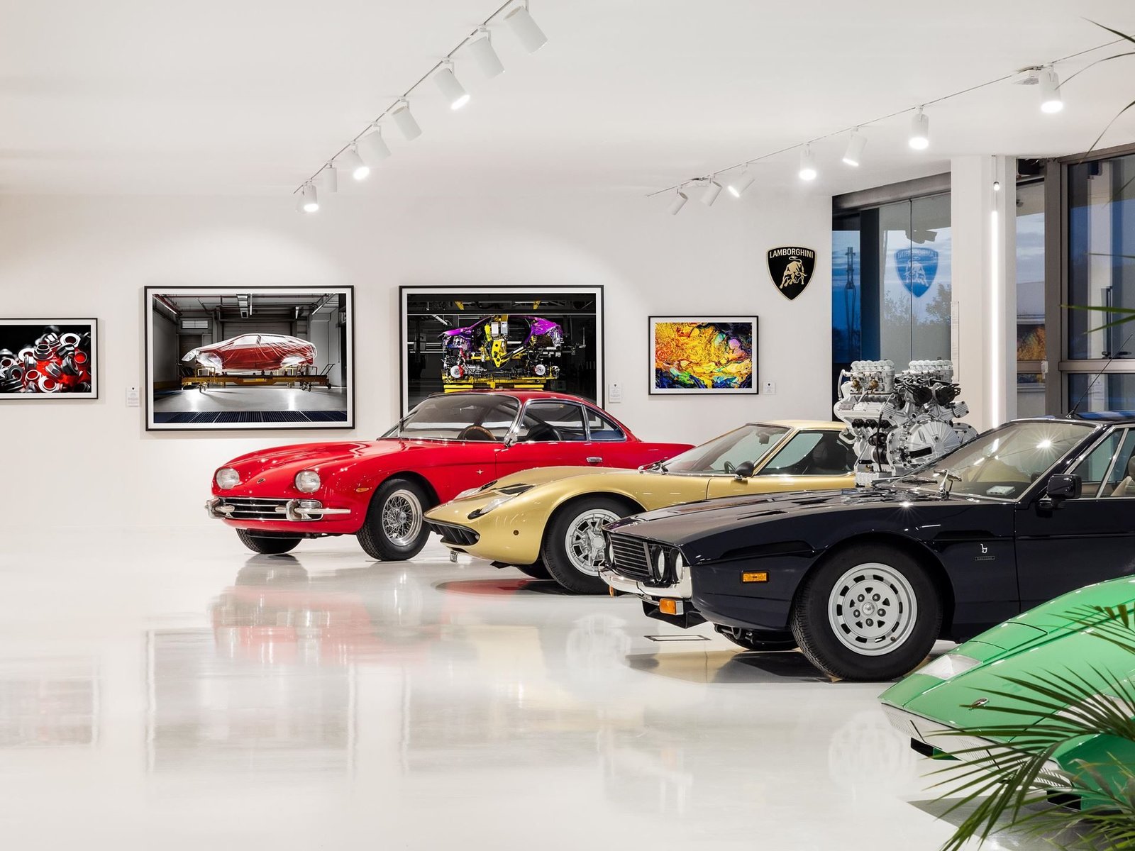 Classic Lamborghini models including a red 400 GT, gold Miura, blue Jarama, and green Urraco displayed alongside framed industrial photography at the Automobili Lamborghini Museum