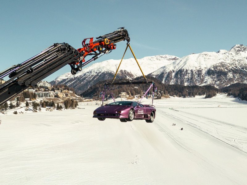 Purple Lamborghini Diablo SE30 suspended by crane above the frozen landscape of St. Moritz with snow-capped mountains in the background