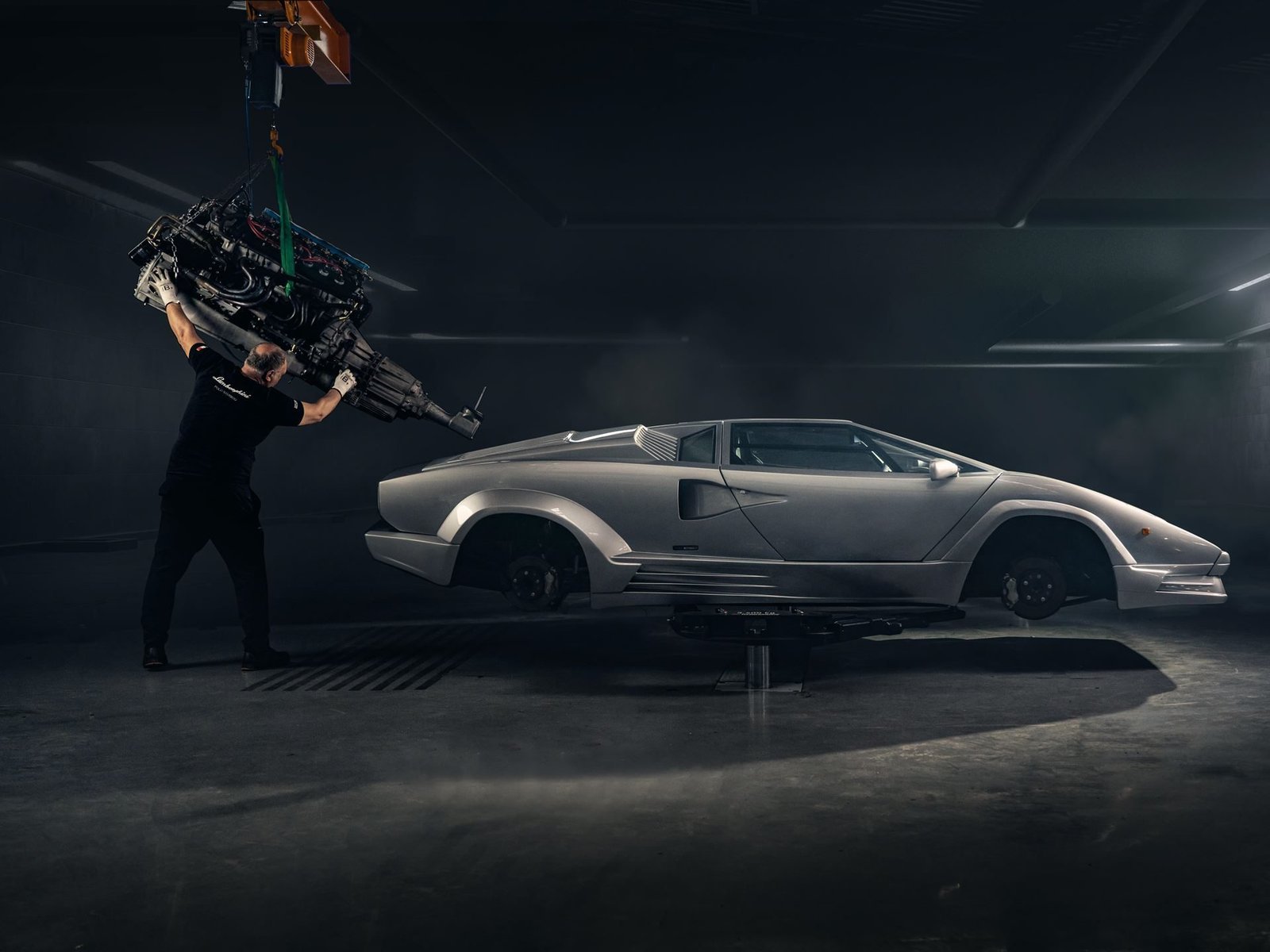 A Polo Storico technician lowers a V12 engine into a silver Lamborghini Countach chassis during restoration