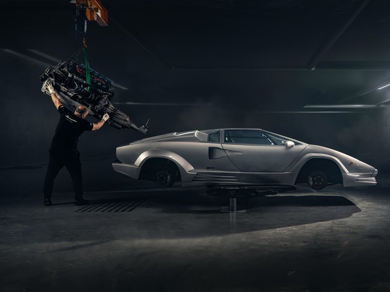 A Polo Storico technician lowers a V12 engine into a silver Lamborghini Countach chassis during restoration