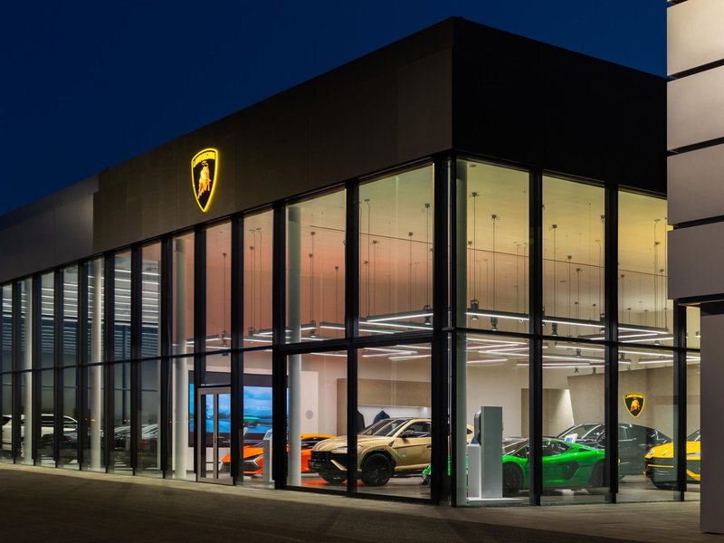 Exterior view of the new Lamborghini Prague showroom in Ořech at dusk, with multiple Lamborghini models visible through the illuminated glass facade
