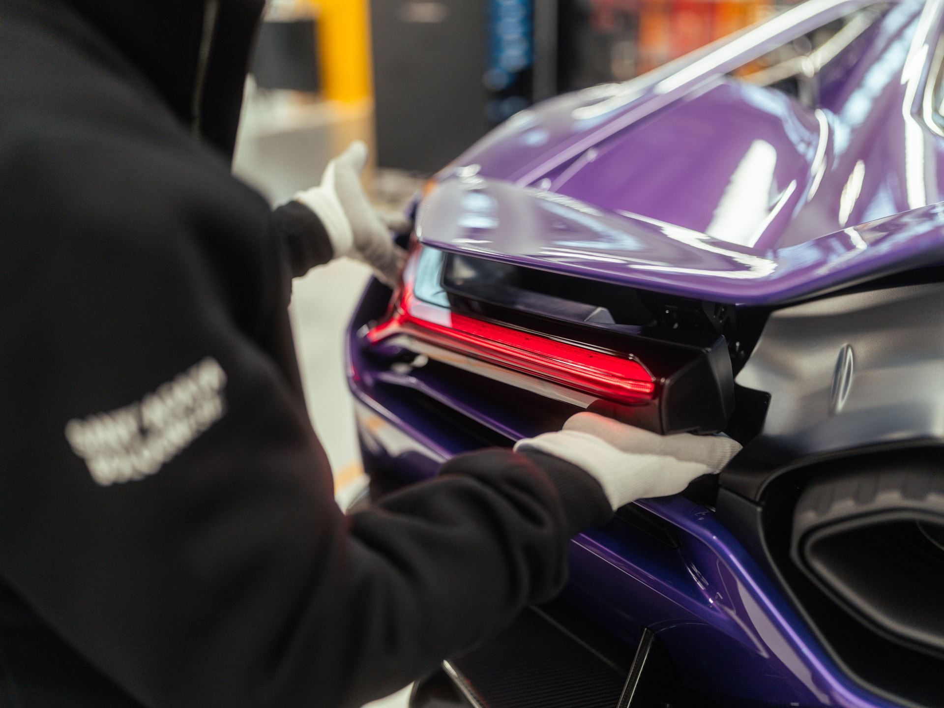 Factory worker in white gloves installing a taillight assembly on a purple lamborghini revuelto on the production line